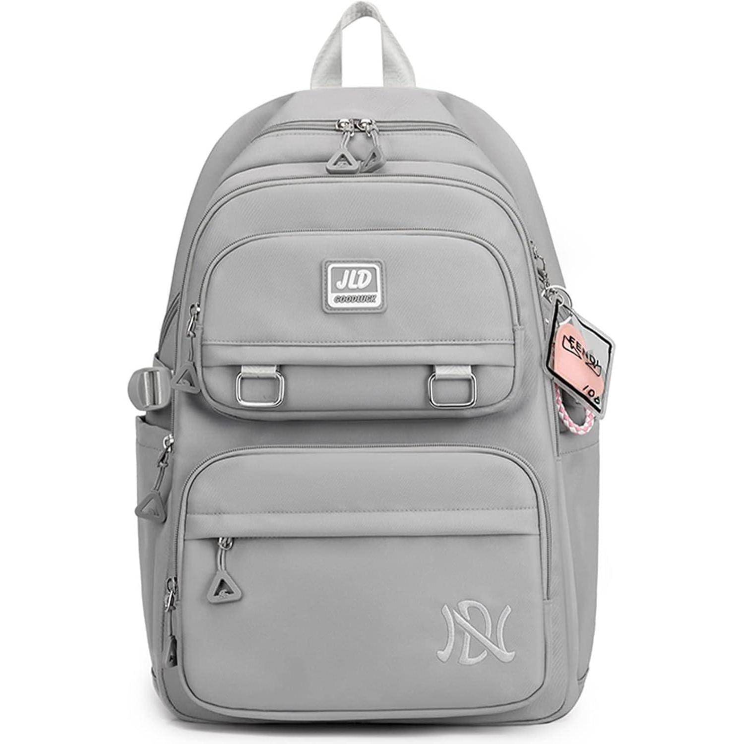 Ein grauer Rucksack mit mehreren Fächern und einer Vordertasche, versehen mit einem Abzeichen und einem kleinen rosa Anhänger am Reißverschluss.