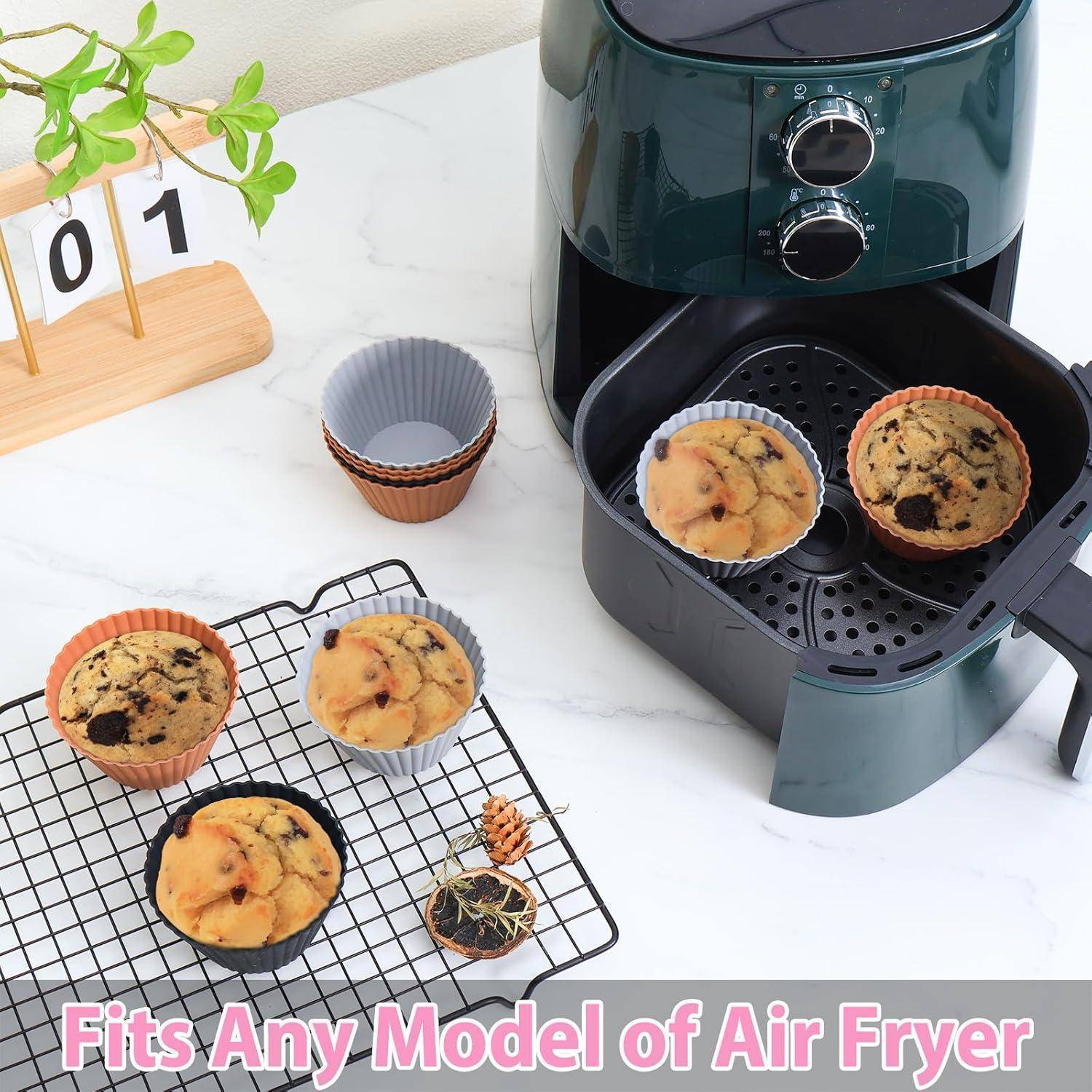 Ein moderner Heißluftfritteur mit Muffins im Inneren und auf einem Rack in der Nähe einer Theke. Text am unteren Rand liest sich: 