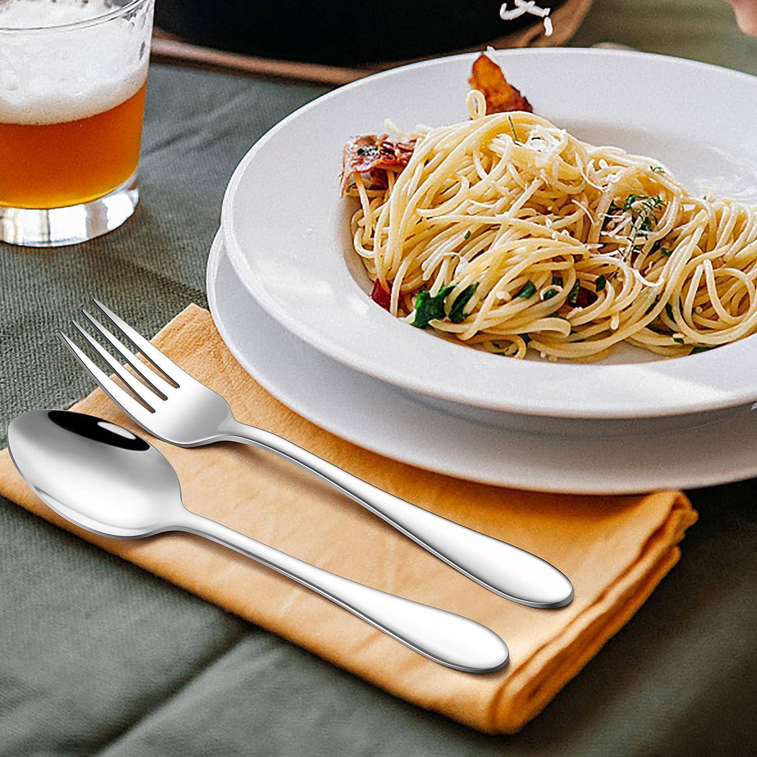 Ein Teller Spaghetti mit Kräutern und Tomaten steht auf einem Tisch neben einem Bierglas und Besteck, das auf einer gefalteten Serviette liegt.