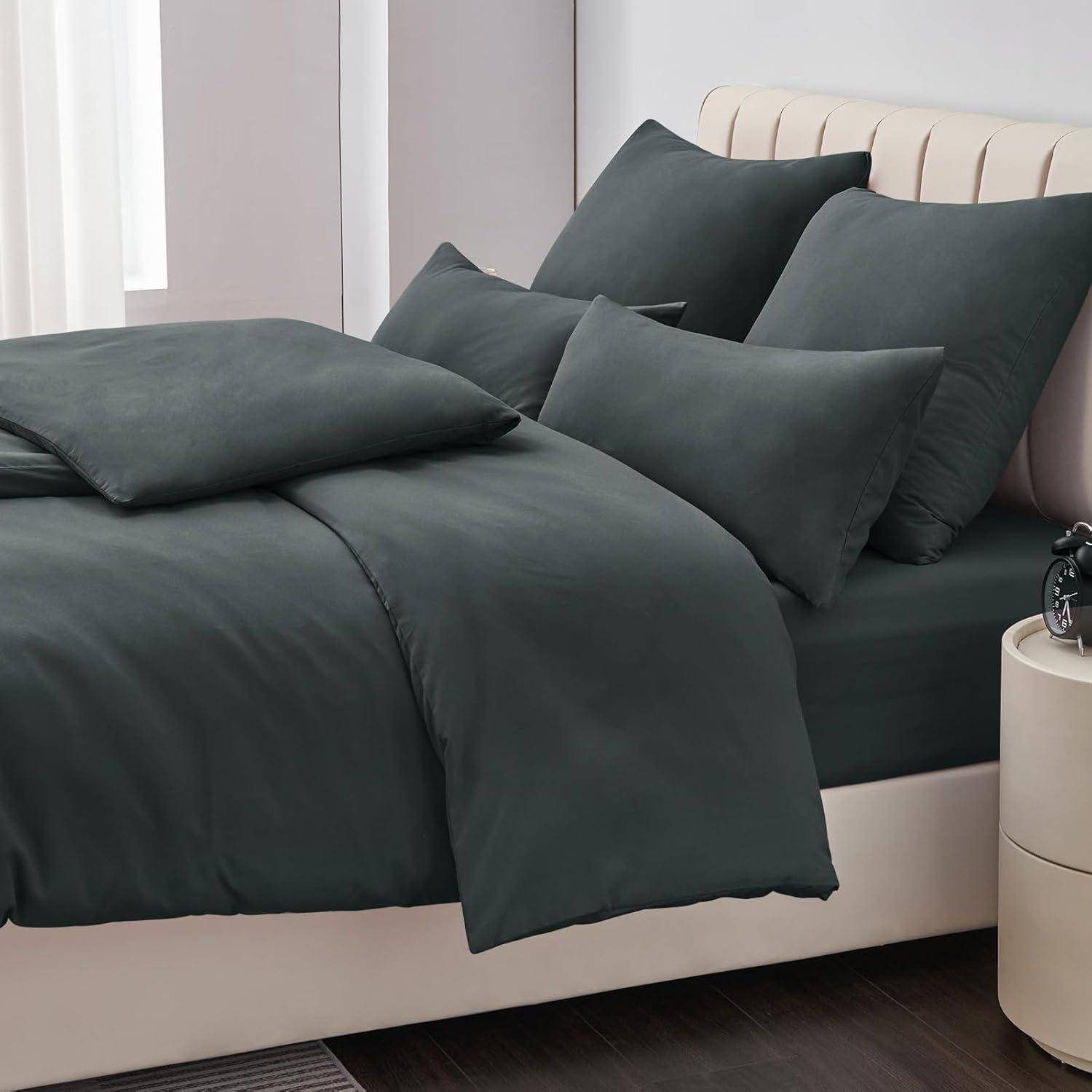 Ein ordentlich gemachtes Bett mit dunkelgrauen Laken, Kissen und Bettdecke in einem modernen Raum, neben einem kleinen Nachttisch ohne sichtbare Gegenstände.