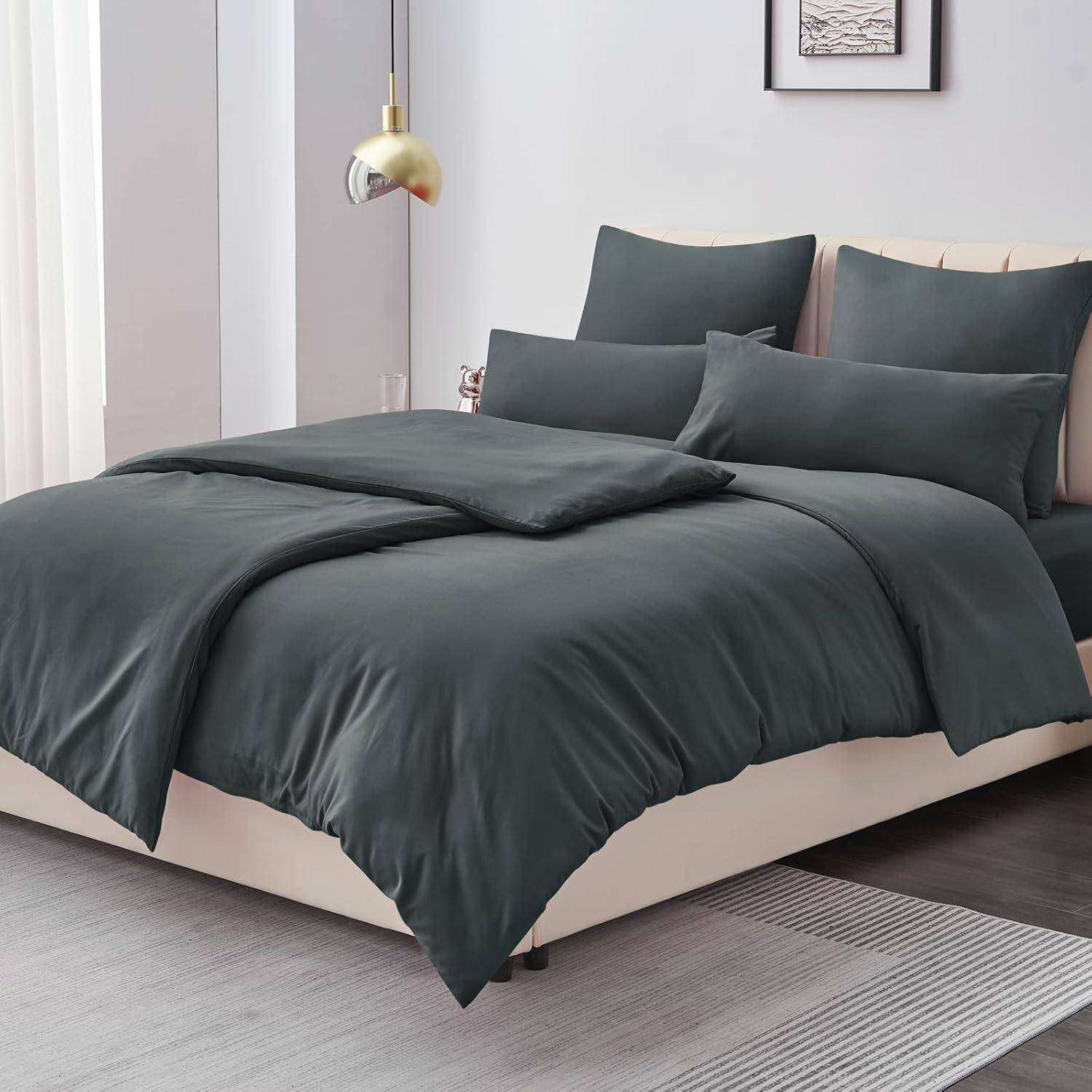 Ein ordentlich gemachtes Bett mit dunkelgrauer Bettwäsche, zwei aufrecht stehenden Kissen und zwei flach liegenden Kissen; eine kleine Lampe an der Seite und gerahmte Kunstwerke darüber.