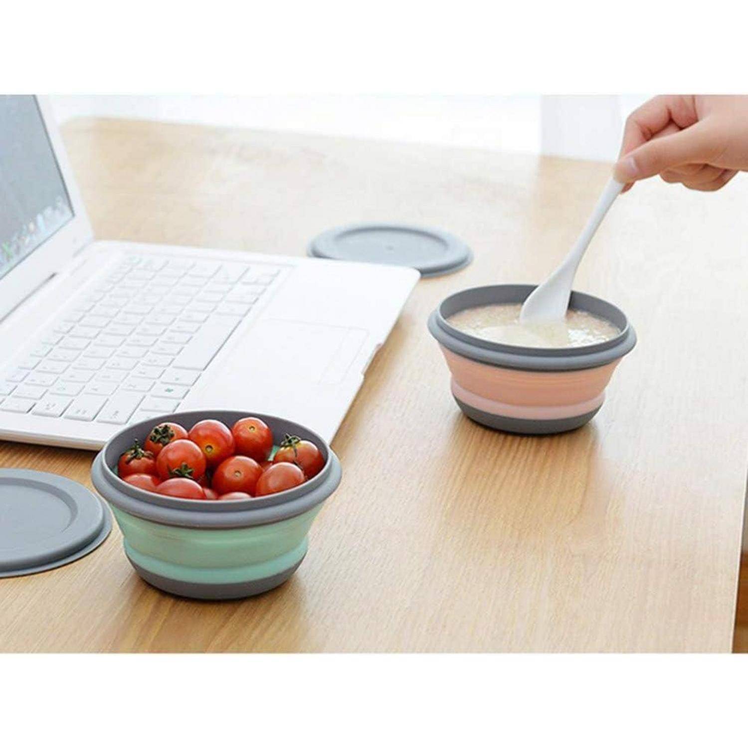 Ein Laptop liegt geöffnet auf einem Holztisch neben zusammenklappbaren Schüsseln. Eine Schüssel enthält Tomaten; eine andere wird gerade mit einem Löffel umgerührt.