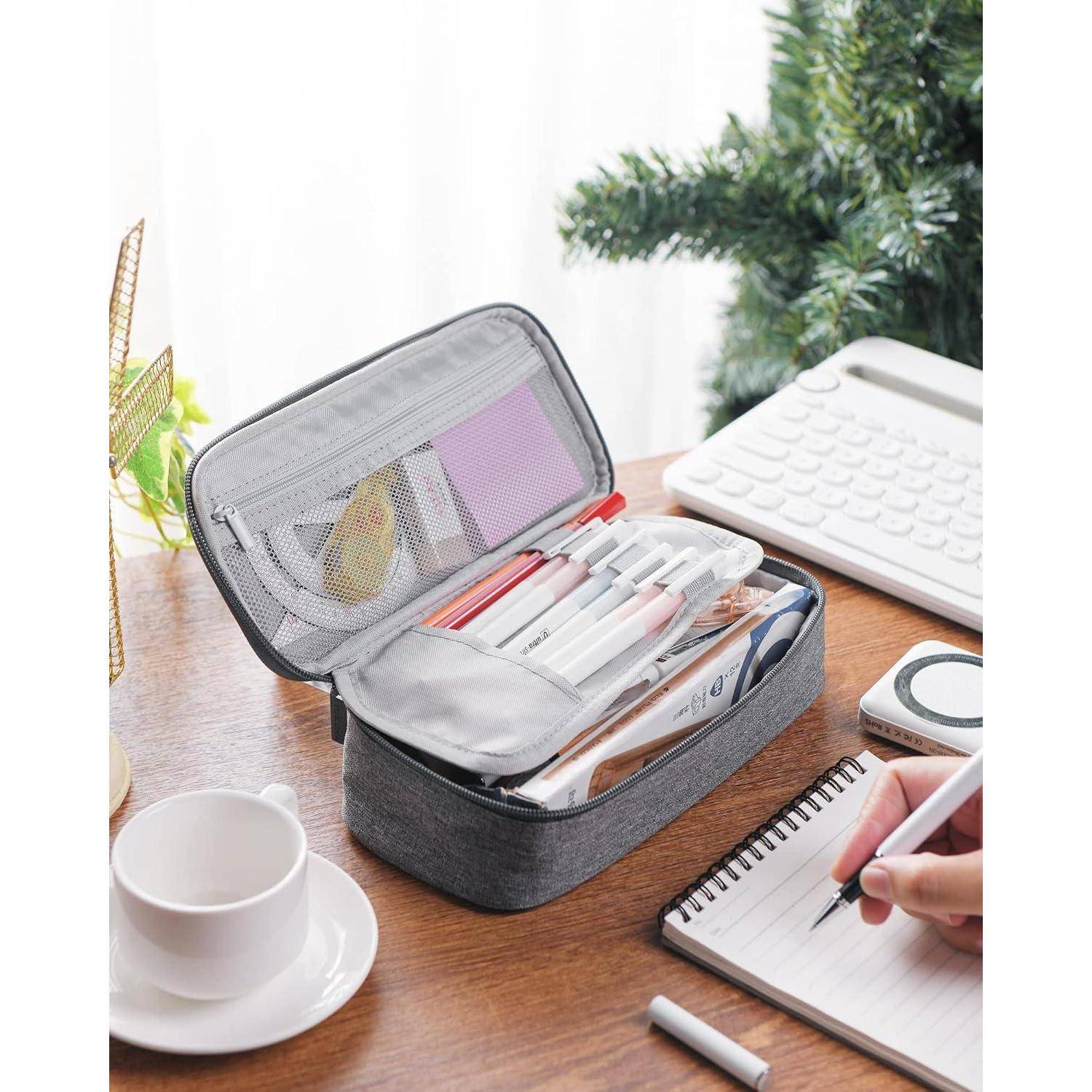 Ein offenes Federmäppchen, gefüllt mit Stiften und Schreibwaren, liegt auf einem Schreibtisch. Eine Person schreibt in ein Notizbuch neben einer Tasse, einem Taschenrechner und einer Topfpflanze.