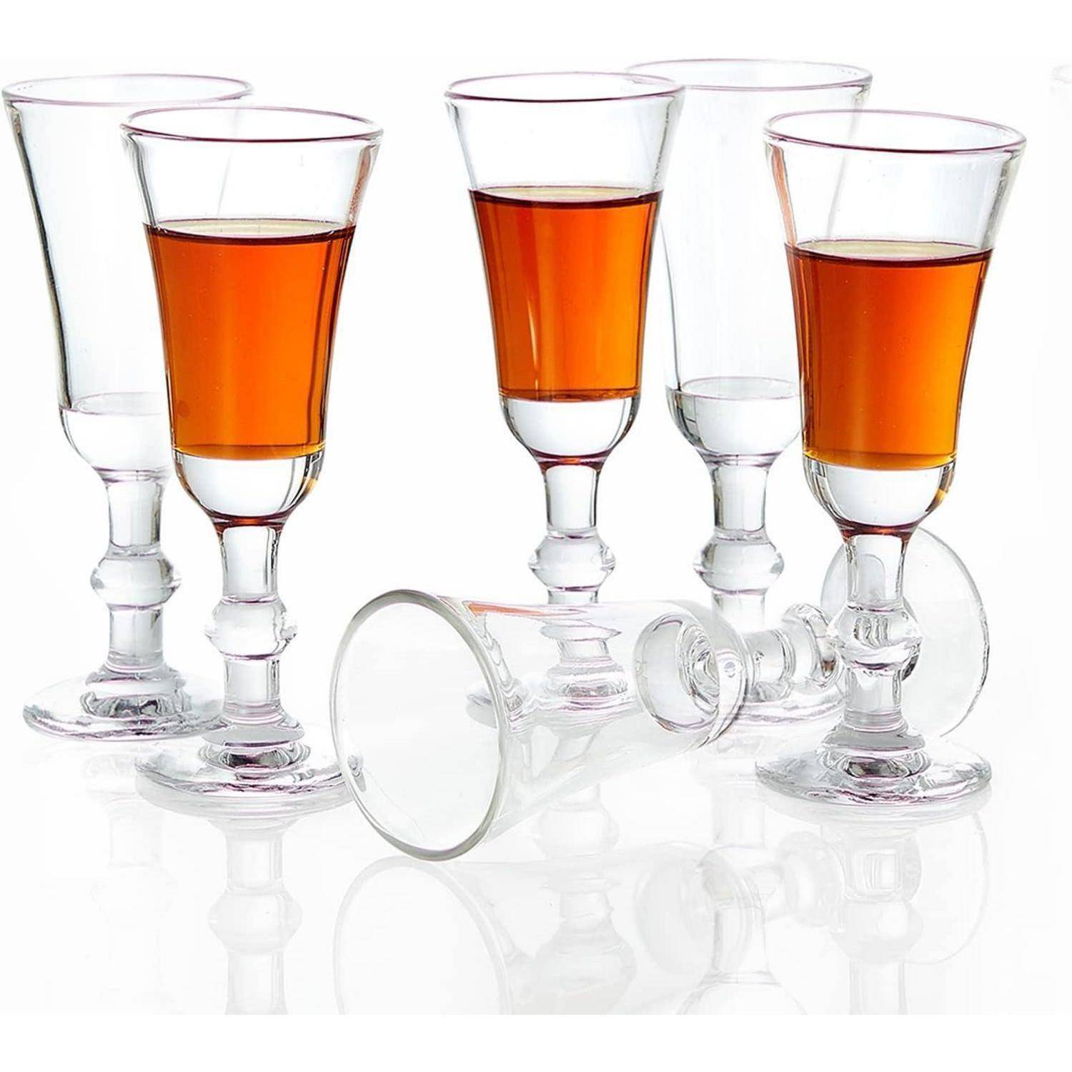 Sechs klare, elegante Gläser, gefüllt mit bernsteinfarbener Flüssigkeit; ein Glas ist umgekippt und deutet auf eine ungezwungene oder festliche Atmosphäre hin.
