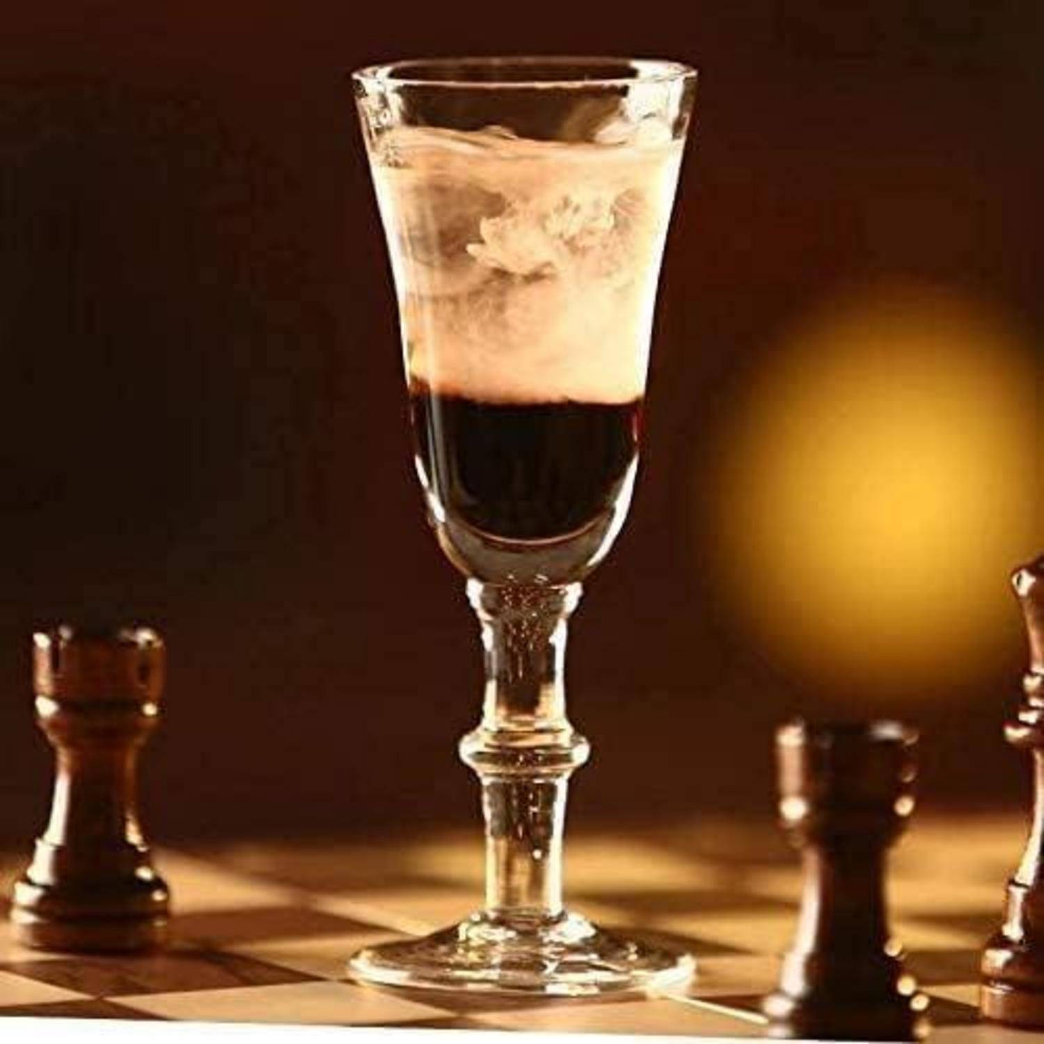 Ein Schachbrett mit Schachfiguren umgibt ein Glas mit einem geschichteten Drink und schafft eine strategische und elegante Atmosphäre.