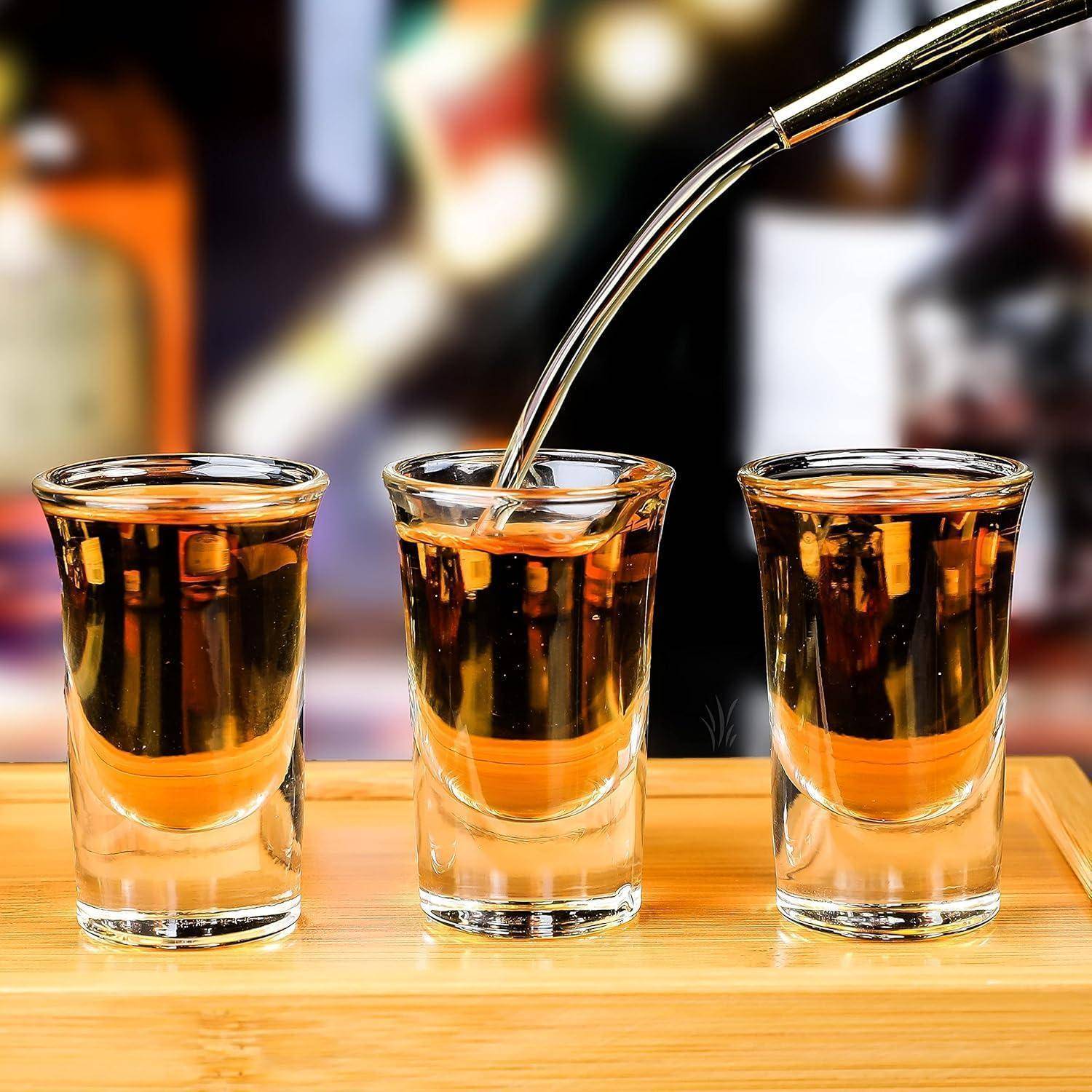 Drei Schnapsgläser, gefüllt mit bernsteinfarbener Flüssigkeit, möglicherweise Whiskey oder einem anderen Spirituosen, mit einem Metallausschenker über dem mittleren Glas.