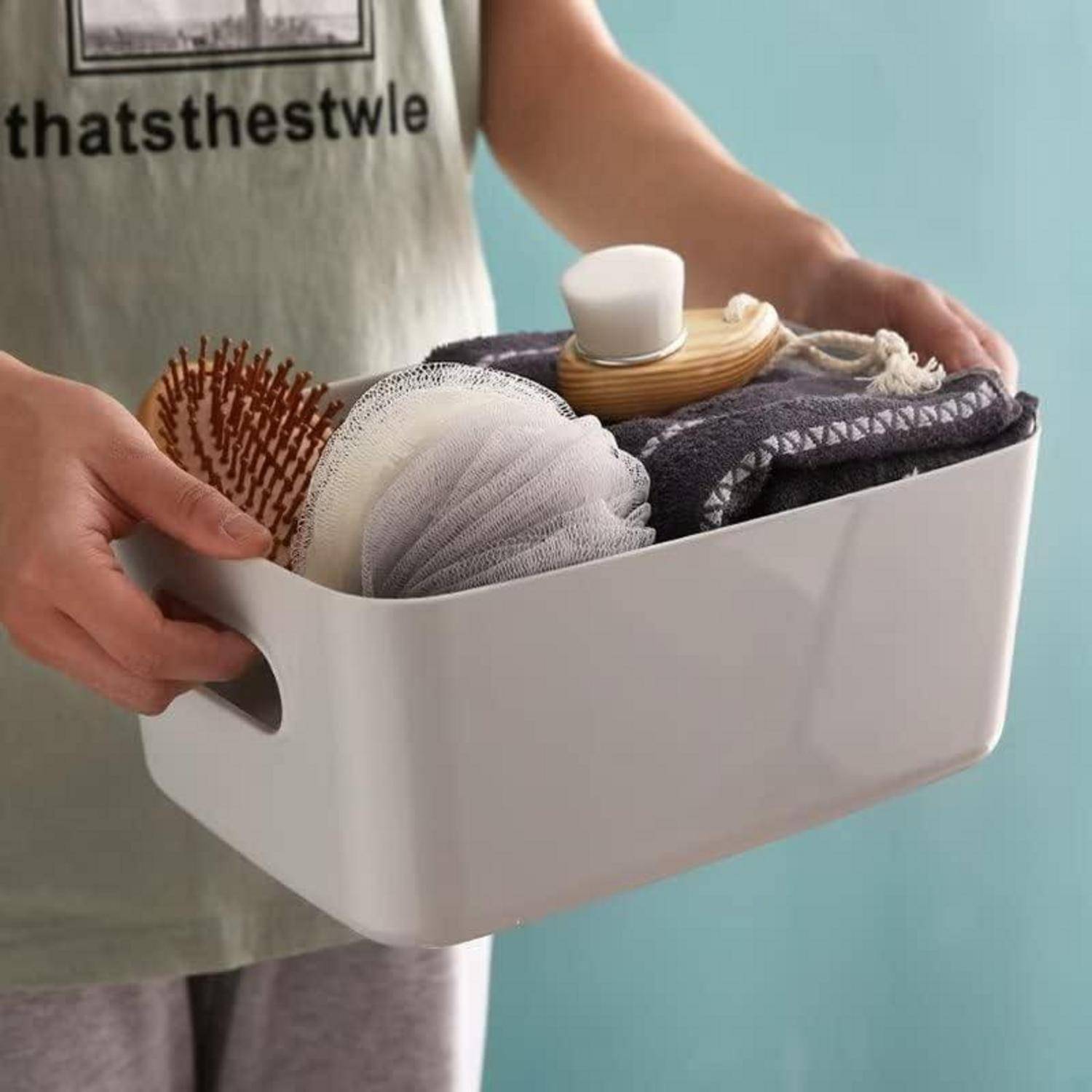 Person, der einen weißen Aufbewahrungsbehälter hält, der mit Körperpflegeprodukten wie einer Holzhaarwürde, einem Schwamm und einem Creme-Tiegel gefüllt ist.