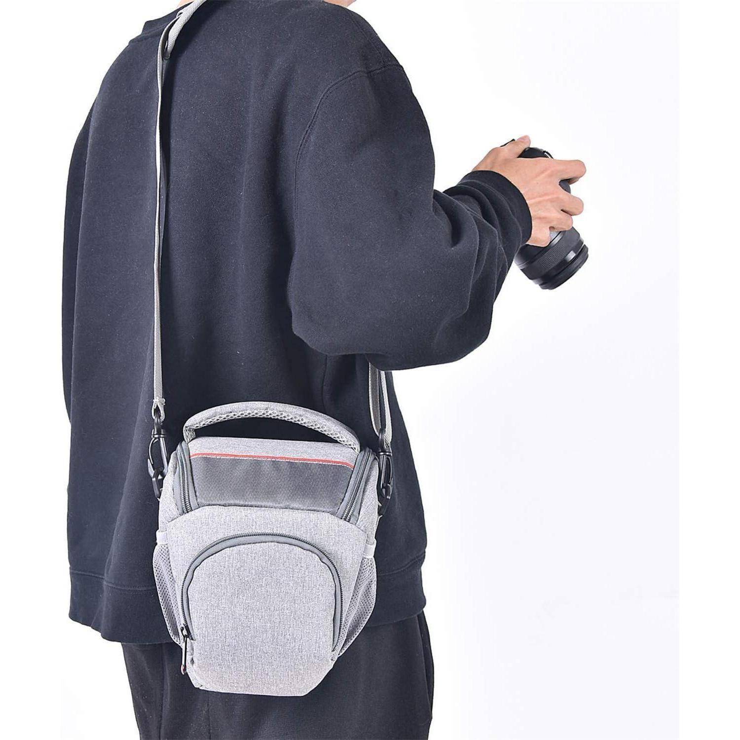 Eine Person in einem dunklen Pullover hält eine Kamera und trägt eine graue Kameratasche über der Schulter.