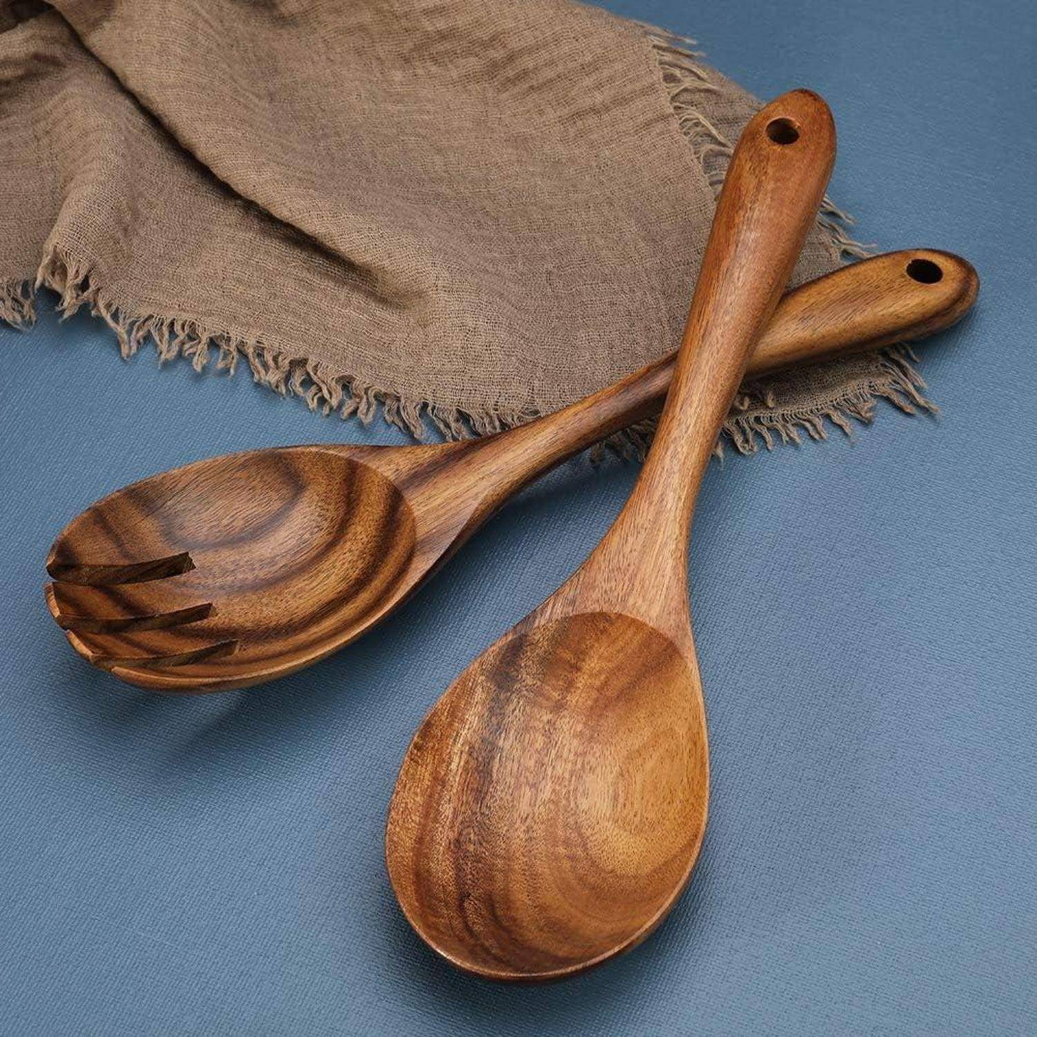 Holz-Salatbesteck auf einer blauen Tischdecke mit einem braunen Stoffserviette im Hintergrund.