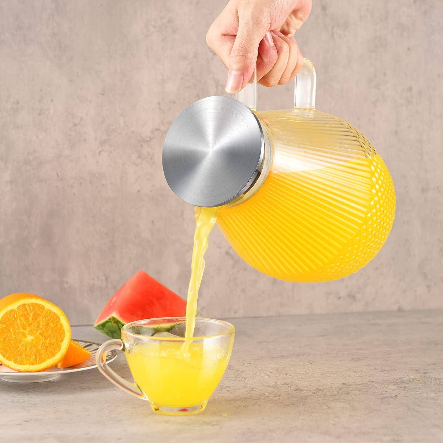 Eine Hand gießt Orangensaft aus einem strukturierten Glaskrug in eine kleine Glasschale. Im Hintergrund liegen Orangen- und Wassermelonenscheiben.