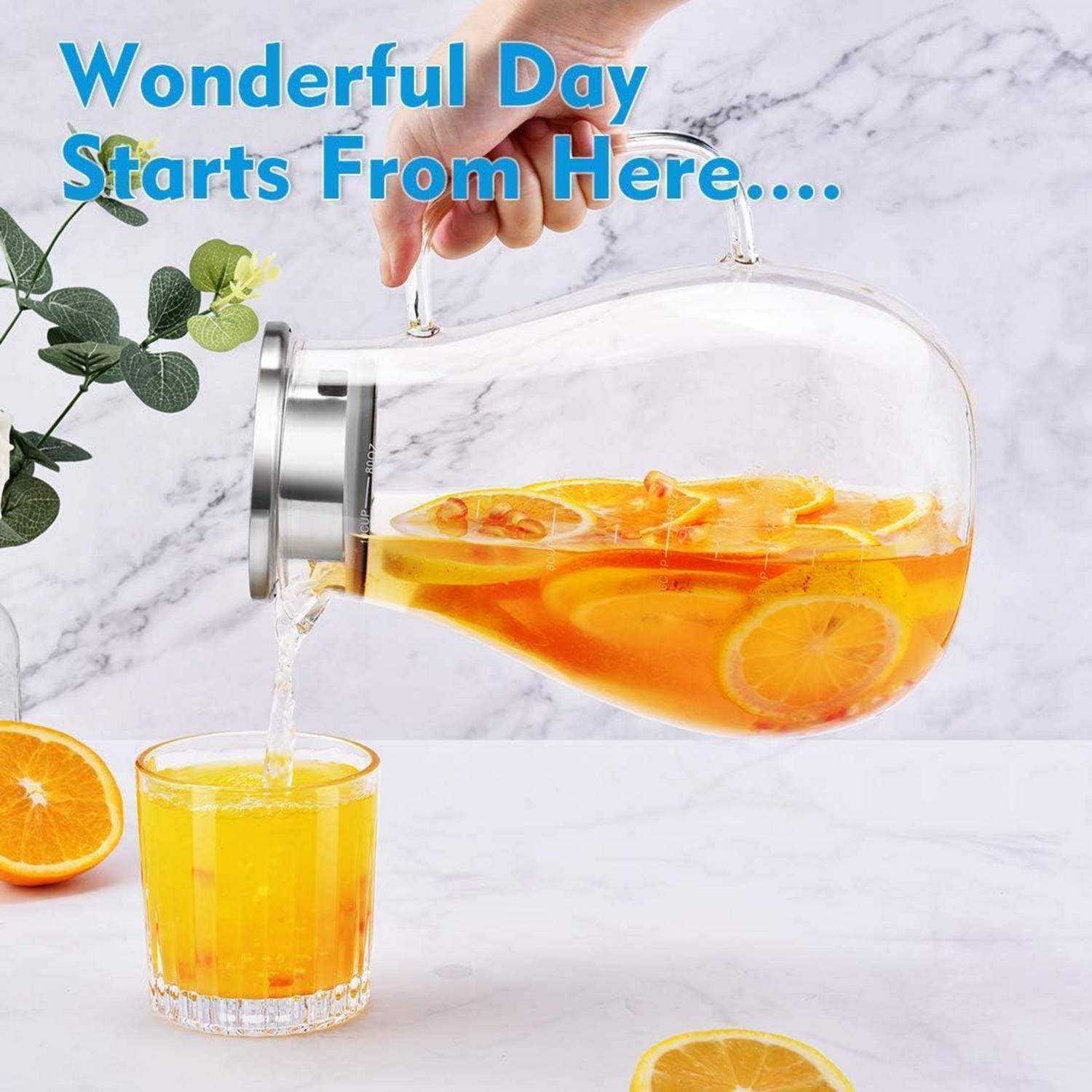 Eine Glaskanne gießt Orangensaft in ein Glas, umgeben von Orangenscheiben auf einer Marmoroberfläche. Blauer Text sagt: „Ein wunderbarer Tag beginnt hier....