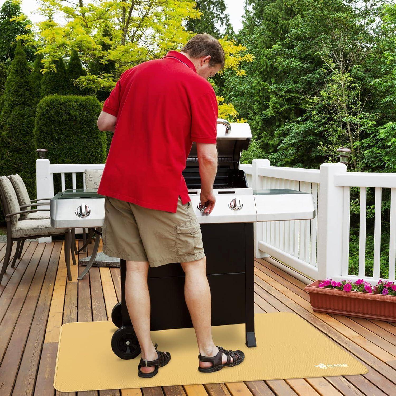 Ein Mann in einem roten Hemd und khakifarbenen Shorts grillt auf einem Barbecue auf einer Holzterrasse, umgeben von Bäumen.
