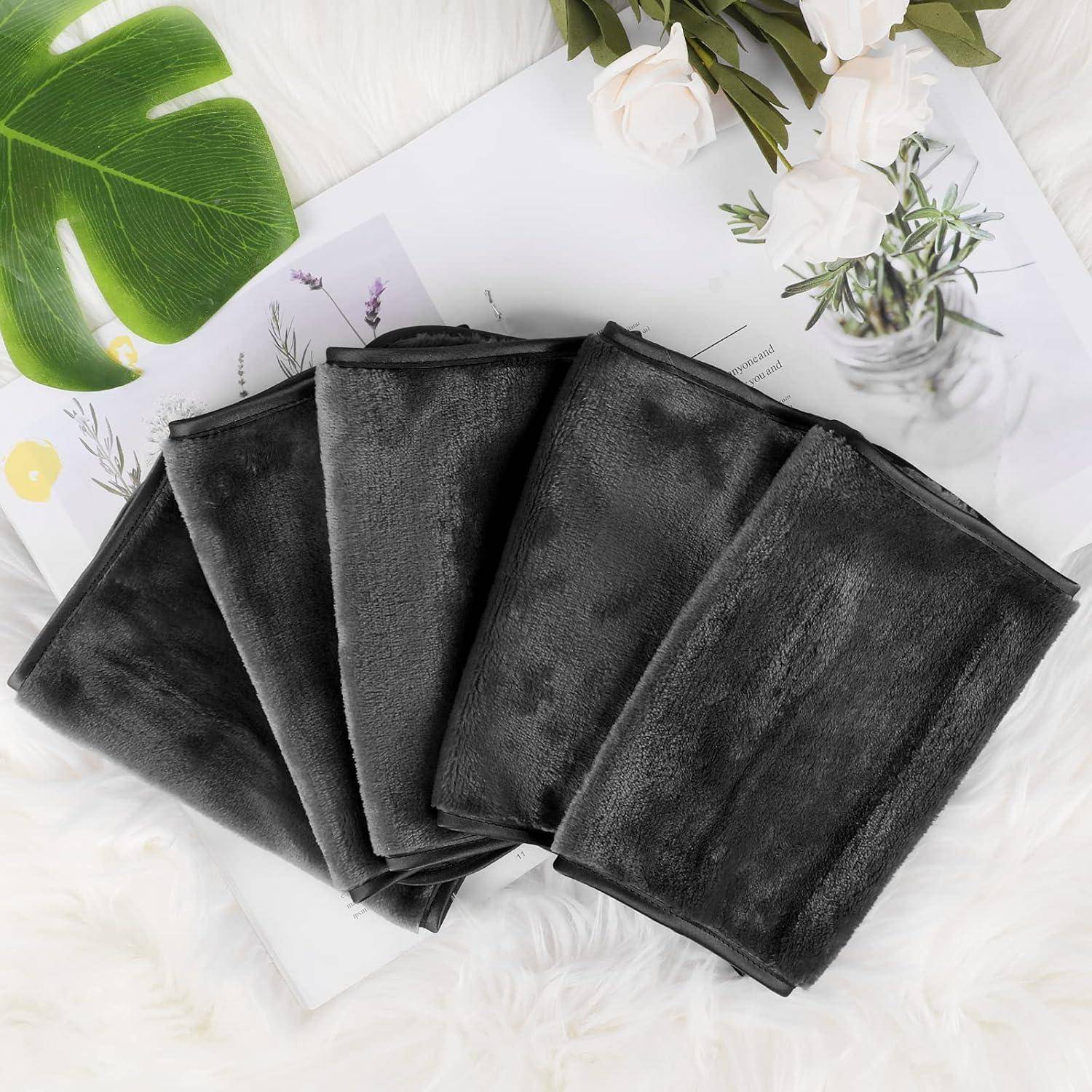 Schwarze Handtücher gefaltet und auf einer hellen Oberfläche angeordnet, mit einem grünen Blatt und einer Vase mit weißen Blumen in der Nähe.