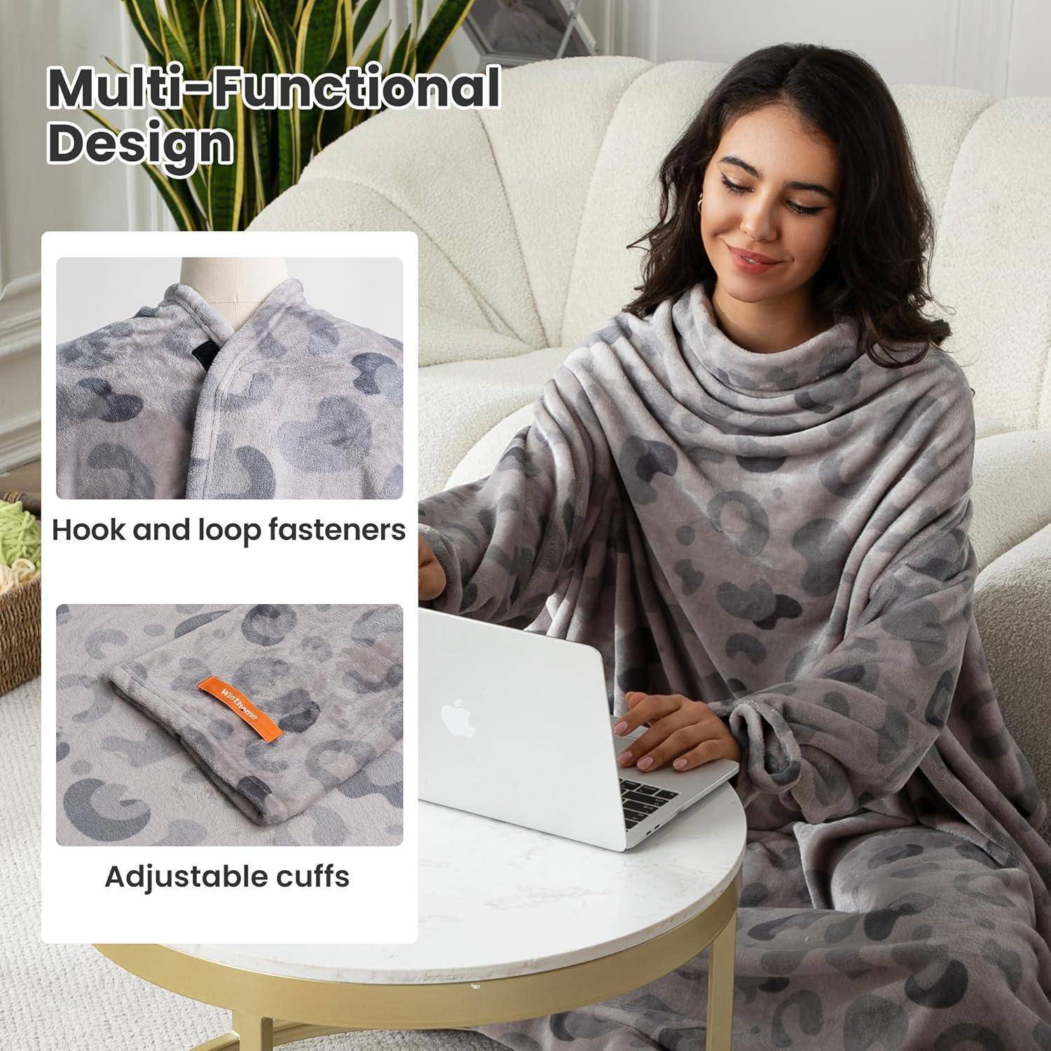 Eine Person, die eine weiche, gemusterte Decke mit verstellbaren Ärmelbündchen und Klettverschlüssen trägt, sitzt auf einem Sofa und arbeitet an einem Laptop.