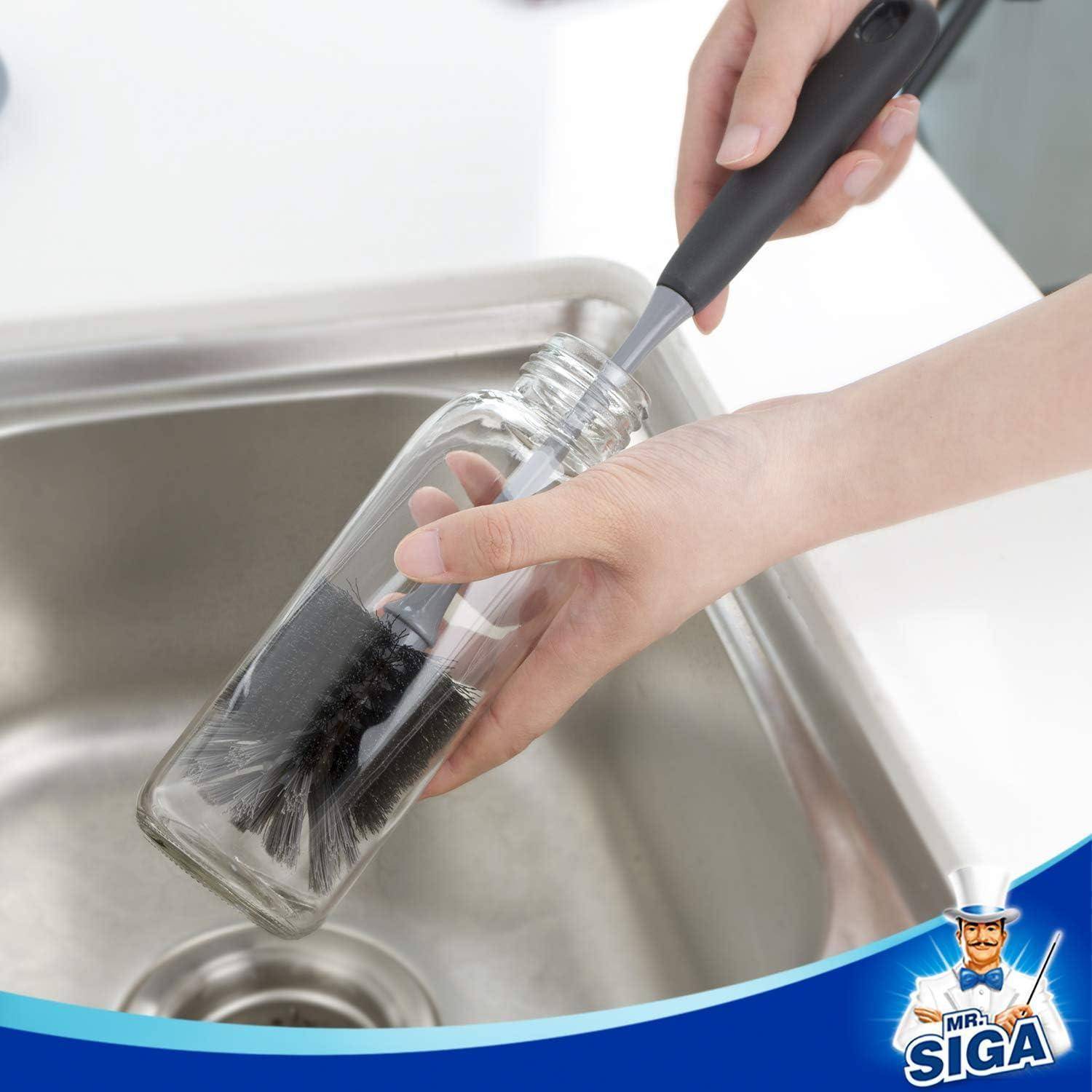 Eine Hand, die die Innenseite einer Glasflasche mit einer langstieligen Bürste über einem Metalllavabo reinigt. Das Mr. Siga-Logo ist in der Ecke sichtbar.