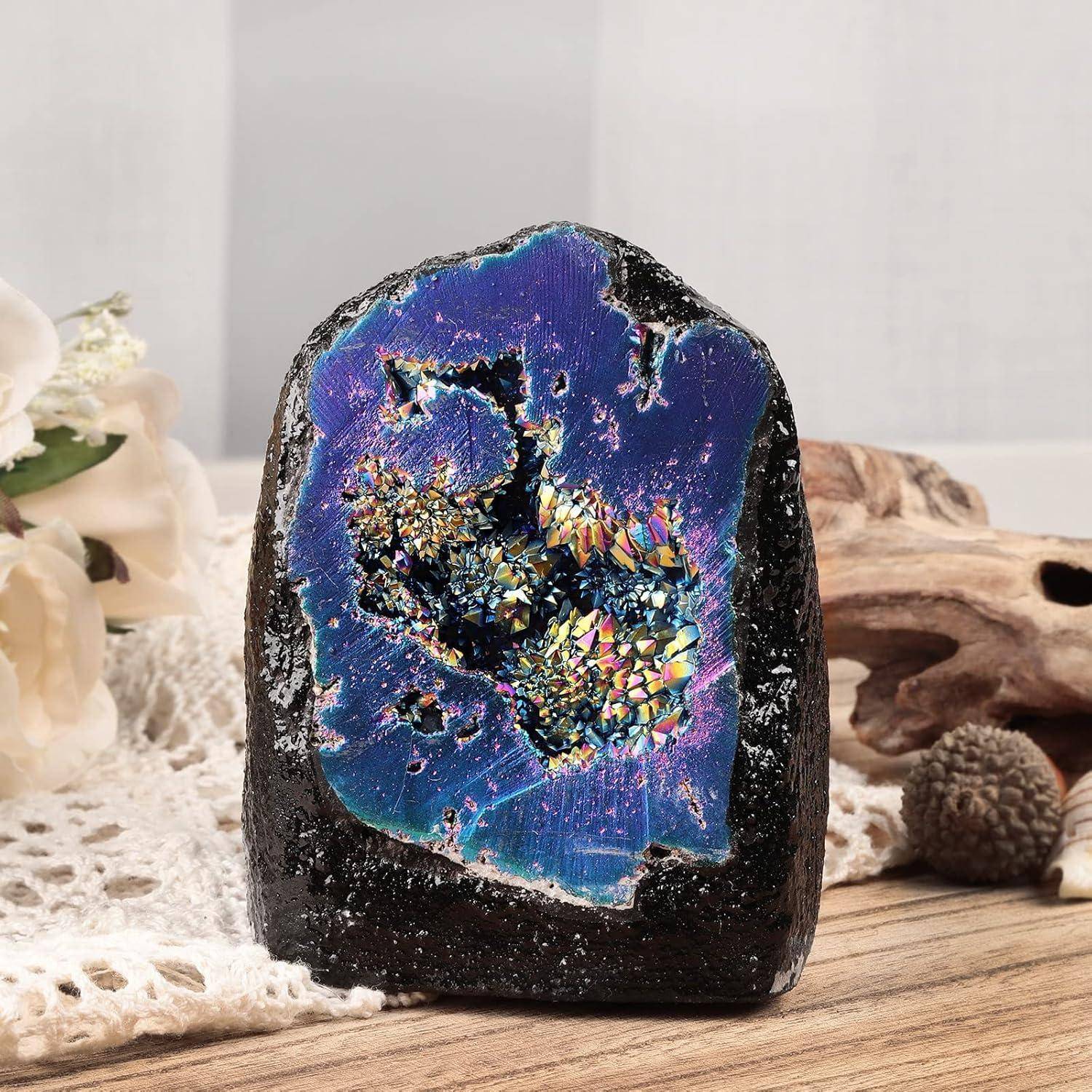 Ein mehrfarbiger Druzy-Geode-Stein ruht auf einer Holzoberfläche, umgeben von weichen dekorativen Elementen, die seine lebendigen Kristalle zur Geltung bringen.