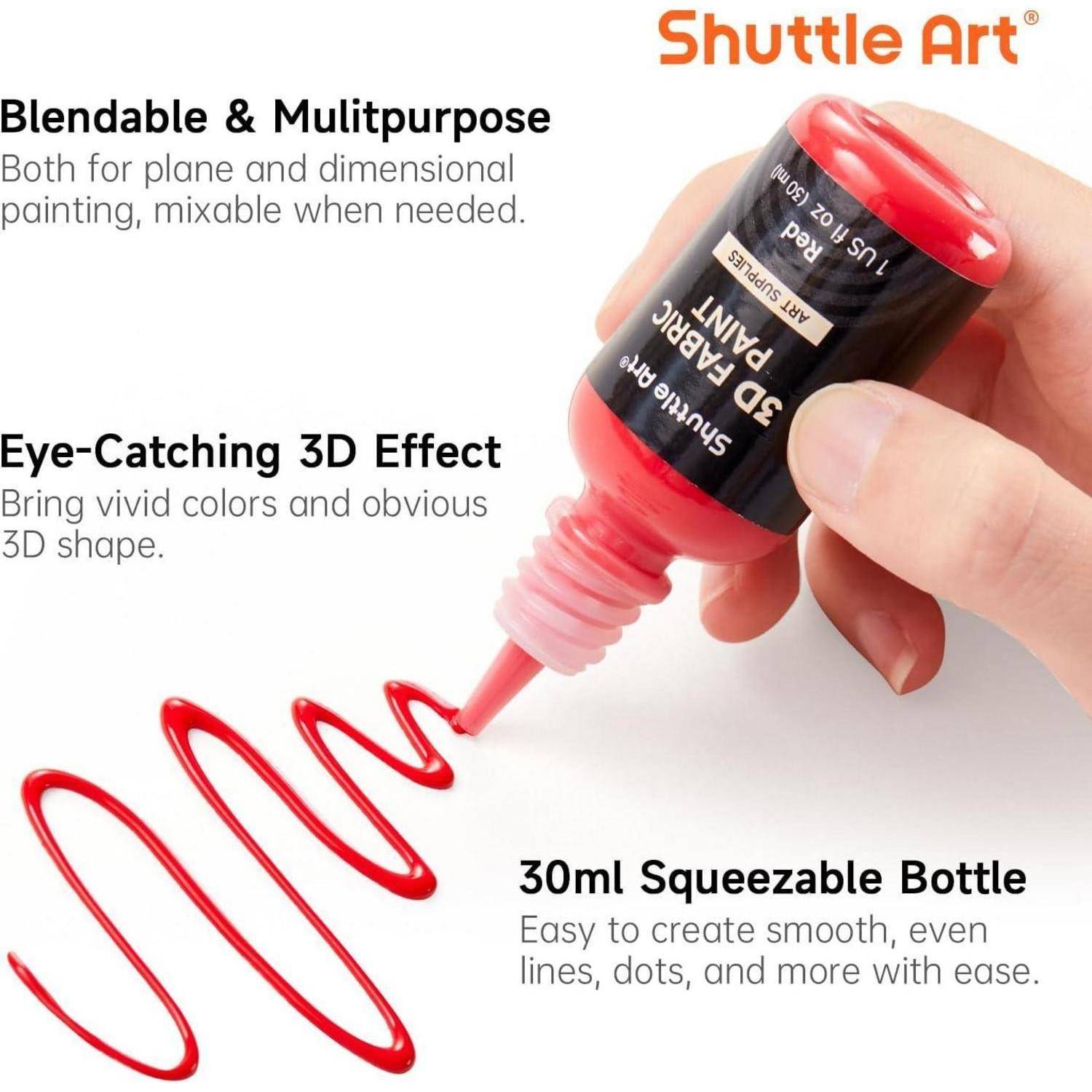 Nahaufnahme einer Hand, die eine rote Shuttle Art 3D-Stoffmalfarbe-Flasche hält und eine Linie Farbe herausquetscht. Der Text betont die lebendige Farbe und vielseitige Verwendungsmöglichkeiten.