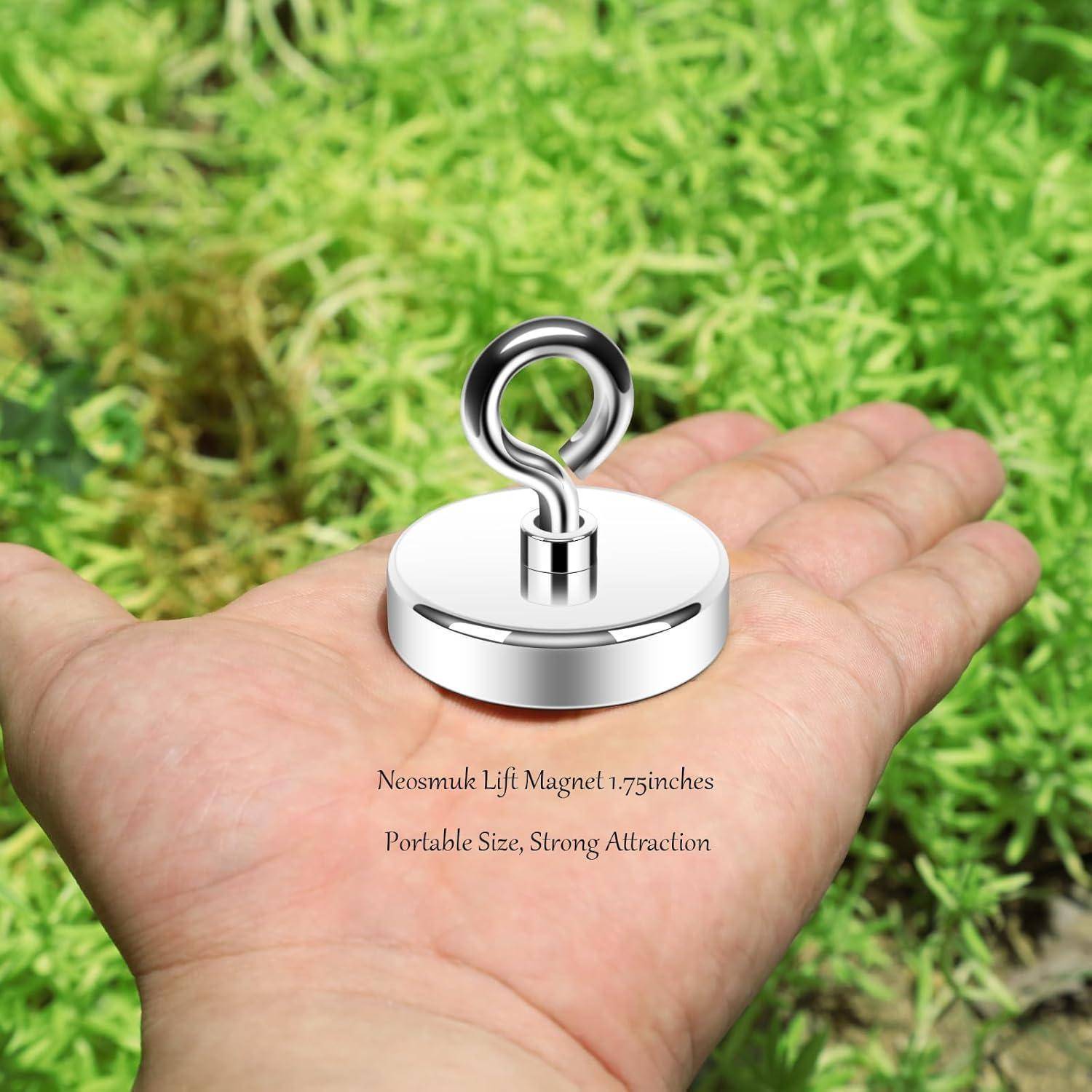 Ein glänzender Metallmagnet mit einer angehängten Schlaufe liegt auf der Handfläche einer Person, über dichtem Grün gehalten. Text lautet: 'Neosmuk Lift Magnet 1,75 Zoll Tragbare Größe, Starke Anziehungskraft'.
