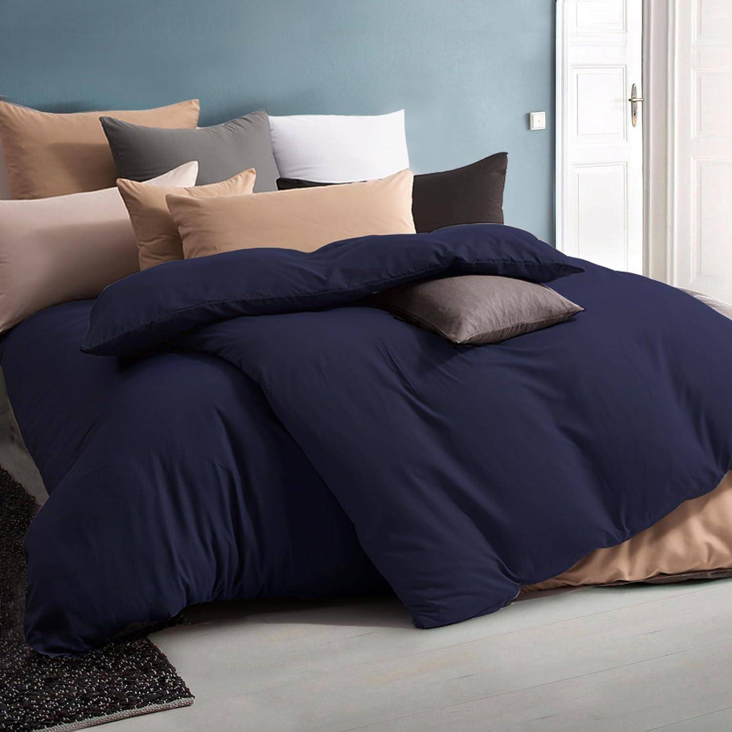 Ein ordentlich gemachtes Bett mit dunkelblauer Bettwäsche und mehreren Kissen in Tönen von Beige, Grau und Weiß, eingebettet in ein sanft beleuchtetes Schlafzimmer.