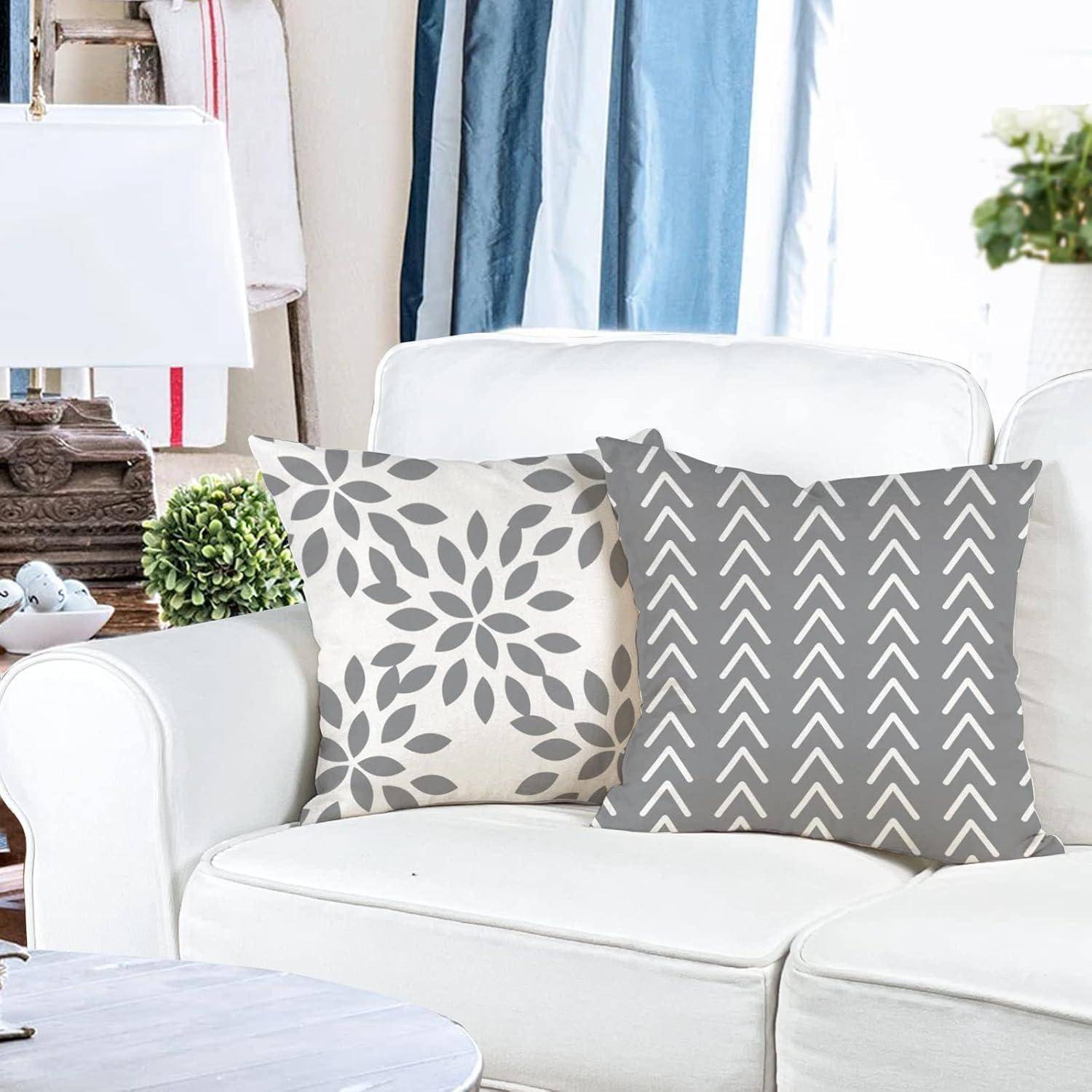 Ein weißes Sofa mit zwei gemusterten Kissen; eines hat ein Blattdesign, das andere ein Zickzackmuster. Eine Lampe und Pflanzen ergänzen die Dekoration.