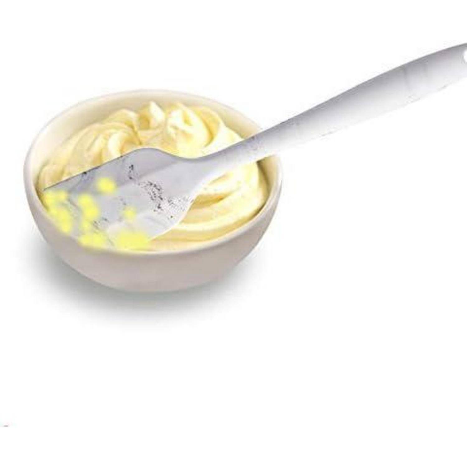 Ein weißer Spatel mit gelben Schlieren liegt in einer Schüssel mit cremiger, blassgelber Mischung, möglicherweise Zuckerguss oder Teig.