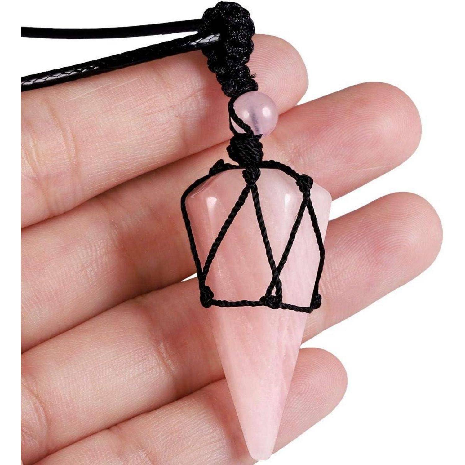 Eine Hand hält ein rosa Pendel, das mit einem schwarzen Kabel umwickelt ist und eine kugelige Perle an der Spitze trägt. Das Pendel ist spitz zulaufend und an einem schwarzen Faden befestigt.