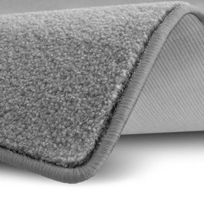 Nahaufnahme eines zusammengelegten grauen Teppichs, der eine strukturierte Schlaufenflor an der Oberfläche und eine glatte, linierte Rückseite darunter offenbart.