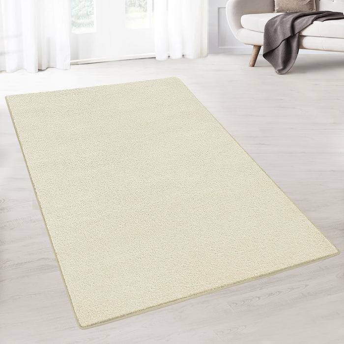 Ein cremefarbener Teppich liegt auf einem Holzboden in einem hellen Raum, wobei ein Teil eines weißen Sofas und ein Vorhang im Hintergrund sichtbar sind.