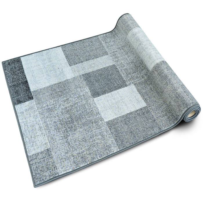 Ein aufgerollter grauer Flickenteppich mit geometrischem Muster, der helle und dunkle Schattierungen mischt und sein modernes Design hervorhebt.