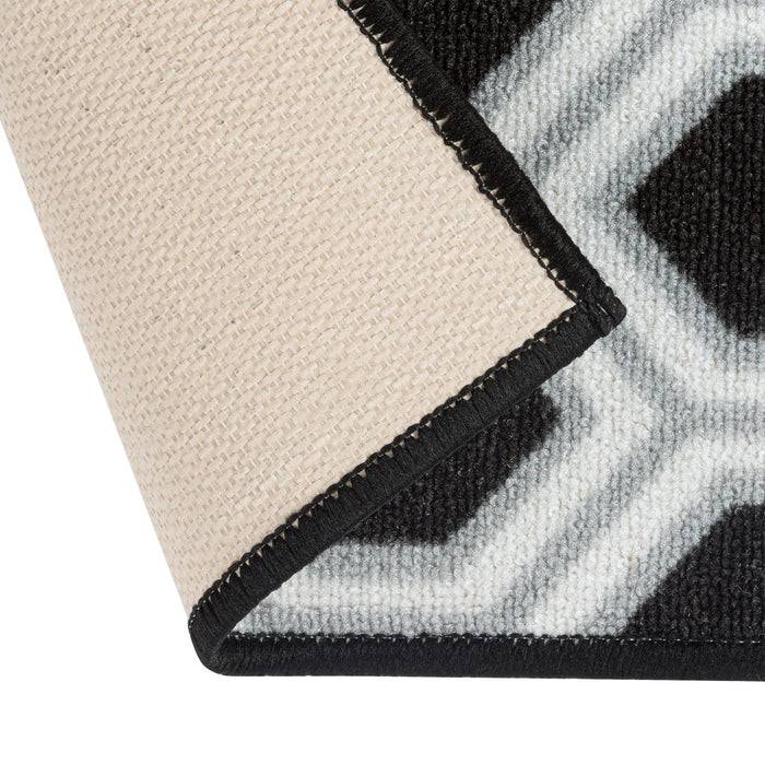 Eine Nahaufnahme eines geometrisch gemusterten Teppichs. Der Rand ist umgeschlagen und zeigt das schwarze und weiße Design auf der Oberseite sowie eine beige Unterseite.