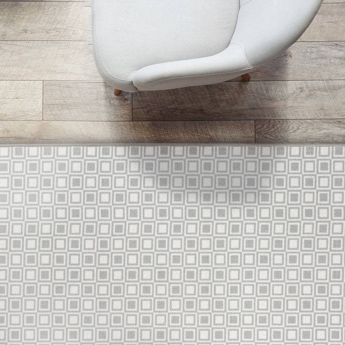 Ein weißer gepolsterter Stuhl auf einem Holzboden neben einem geometrisch gemusterten Teppich.