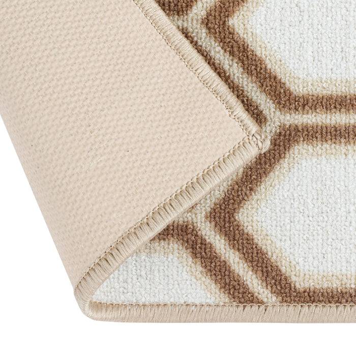 Ein beige Teppich mit sichtbarer umgeschlagener Ecke, der ein geometrisches Sechseckmuster in Braun und Weiß aufweist.