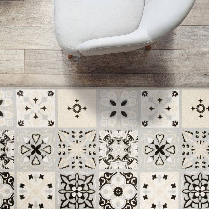 Ein grauer Sessel auf einem Holzboden neben einem gemusterten Teppich mit schwarz-weißen Blumen- und geometrischen Designs.