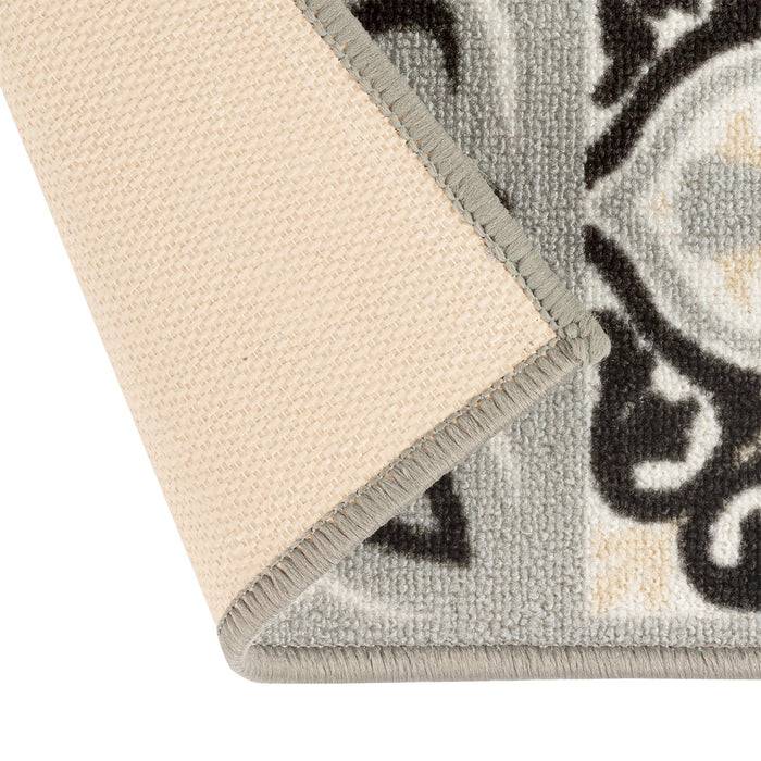 Eine Ecke eines beige-schwarzen gemusterten Teppichs ist nach oben geschlagen und zeigt die geschichtete, strukturierte Gestaltung und kontrastierenden Farben.