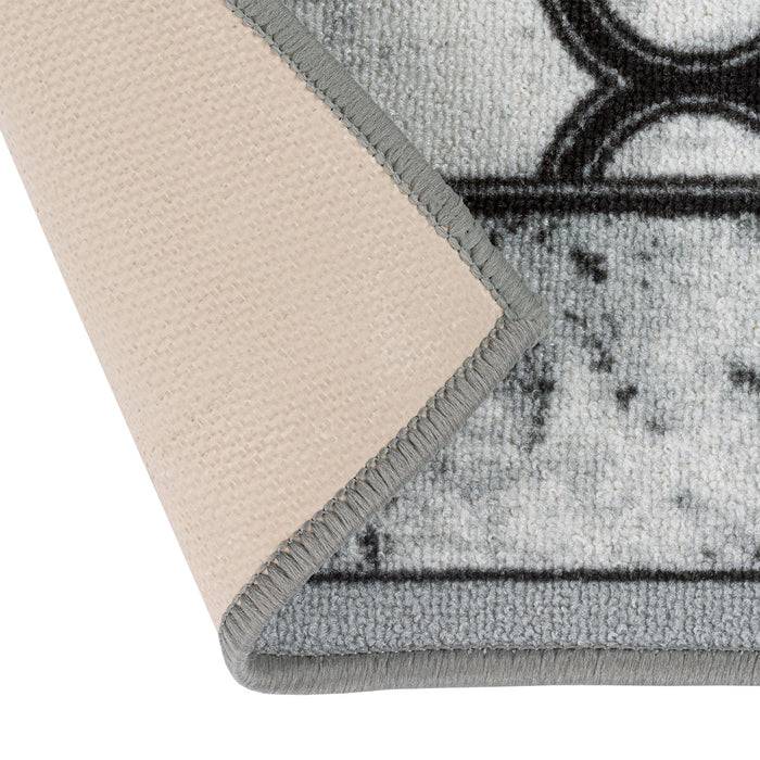 Eine umgeschlagene Ecke eines strukturierten Teppichs in Beige und Grau mit geometrischen Mustern ist zu sehen, wobei die Gewebetextur und die Kantennaht hervorgehoben werden.