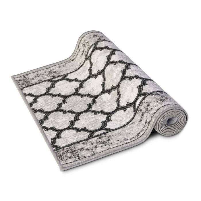 Ein aufgerollter Teppich mit einem geometrischen Muster aus verschachtelten Formen in Schwarz und Weiß. Die Kanten sind leicht abgenutzt.