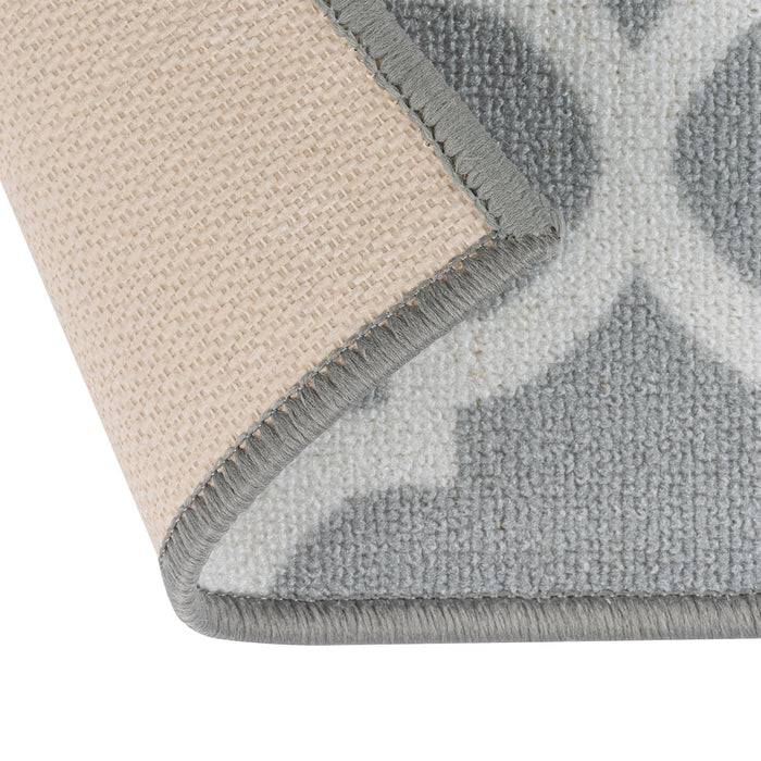 Das Bild zeigt die Ecke eines beige-grauen Teppichs, der umgefaltet ist, um dessen strukturierte Rückseite und gemusterte Vorderseite in einer kreuzförmigen Anordnung zu zeigen.