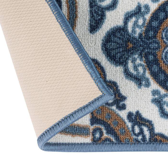 Eine Nahaufnahme einer umgeschlagenen Ecke eines Teppichs, die ein blaues und weißes kompliziertes Blumenmuster mit einer beigen Unterseite und blauer Naht zeigt.