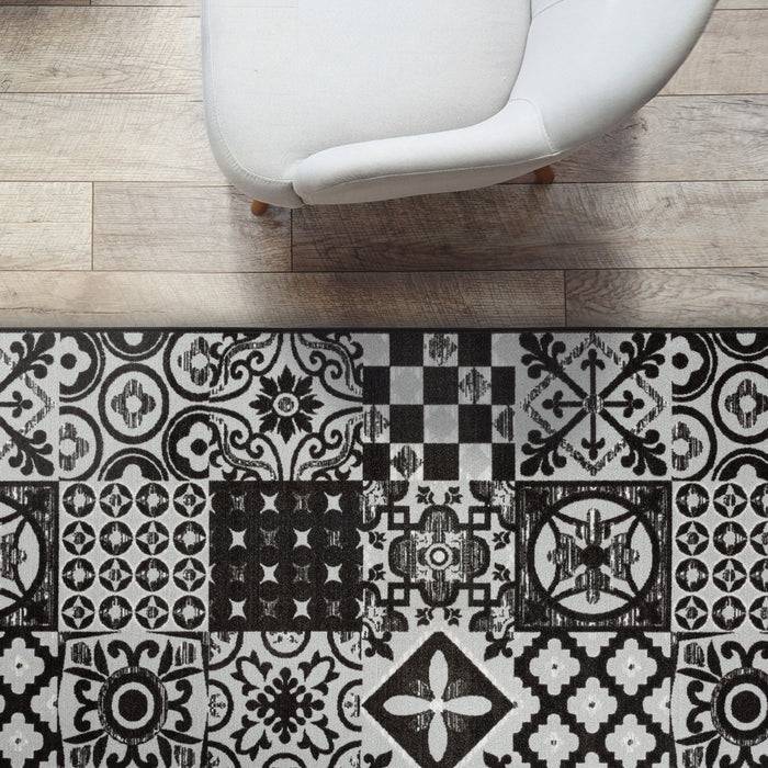 Ein weißer Sessel steht auf einem hellholzfarbenen Boden neben einem schwarz-weißen gemusterten Teppich mit verschiedenen geometrischen Designs.