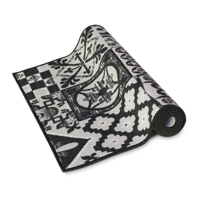 Eine schwarz-weiße gemusterte Yogamatte, teilweise aufgerollt, mit detaillierten Designs einschließlich Blumen, geometrischer Formen und ornamentaler Motive.