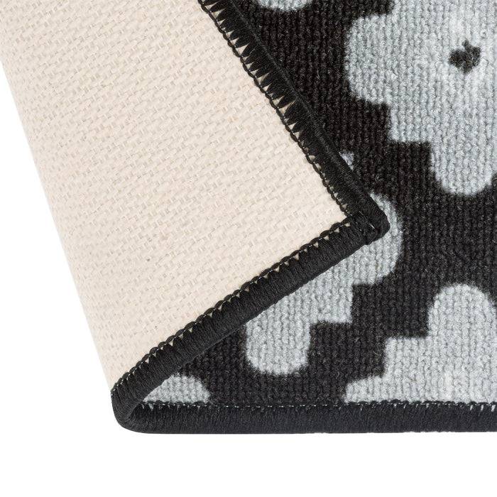 Eine Nahaufnahme einer Ecke eines gewebten Teppichs mit geometrischen schwarzen und weißen Mustern, die die Textur und Stickdetails zeigt.