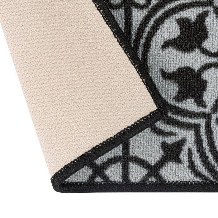 Eine Nahaufnahme einer gemusterten Teppichecke, die umgeschlagen ist und ihre beige Unterseite zeigt. Das Design weist dunkle geometrische Formen auf einem hellen Hintergrund auf.