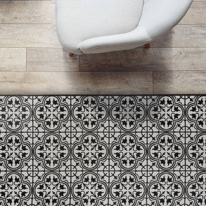 Ein weißer Stuhl steht auf einem gemusterten Boden mit kunstvollen schwarzen und weißen Fliesen, neben einem Holzfußbodenbereich, der einen markanten Kontrast erzeugt.