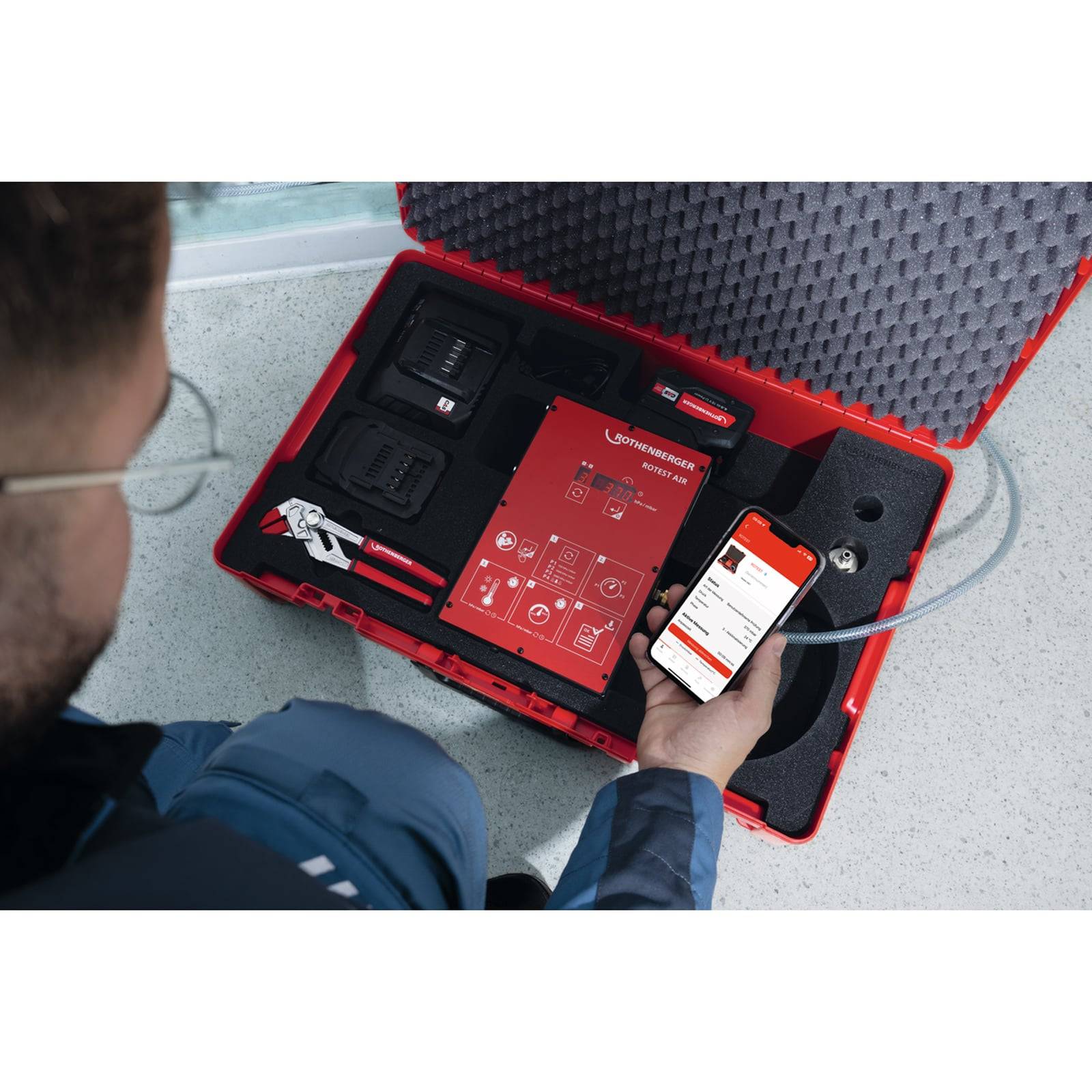 Eine Person nutzt eine mobile Telefon-App, um mit einem roten Gehäuse mit elektronischen Werkzeugen zu interagieren.