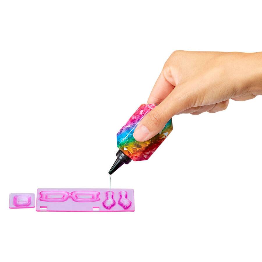 Eine Hand hält einen bunten Flüssigstift über eine rosa Form mit Brille und anderen Formen, was auf eine Bastel- oder Dekorationsaktivität hindeutet.