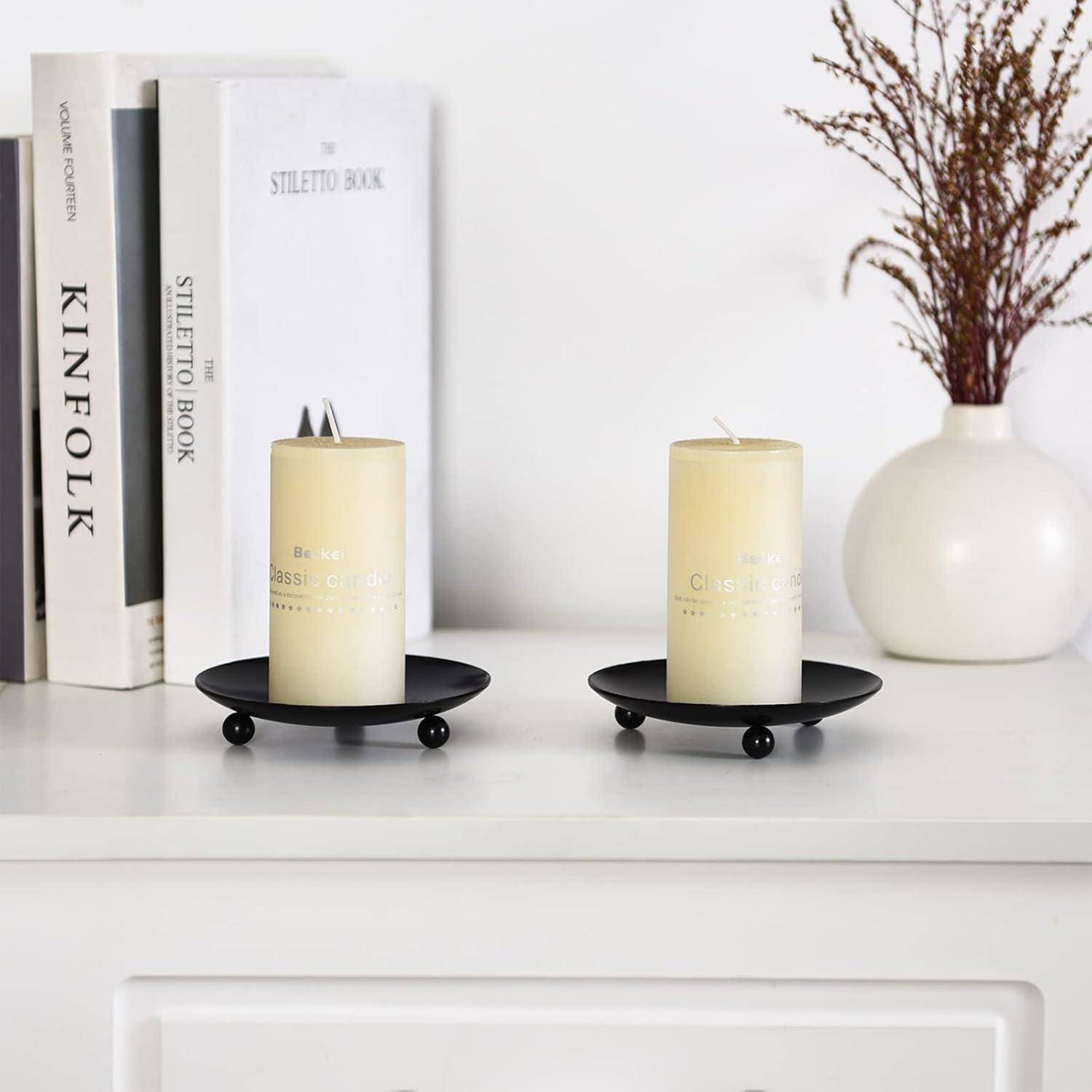 Kerzen auf Haltern ruhen auf einem weißen Schrank, mit Büchern und einer Vase mit Zweigen in der Nähe, die eine minimalistische und gemütliche Dekoration schaffen.