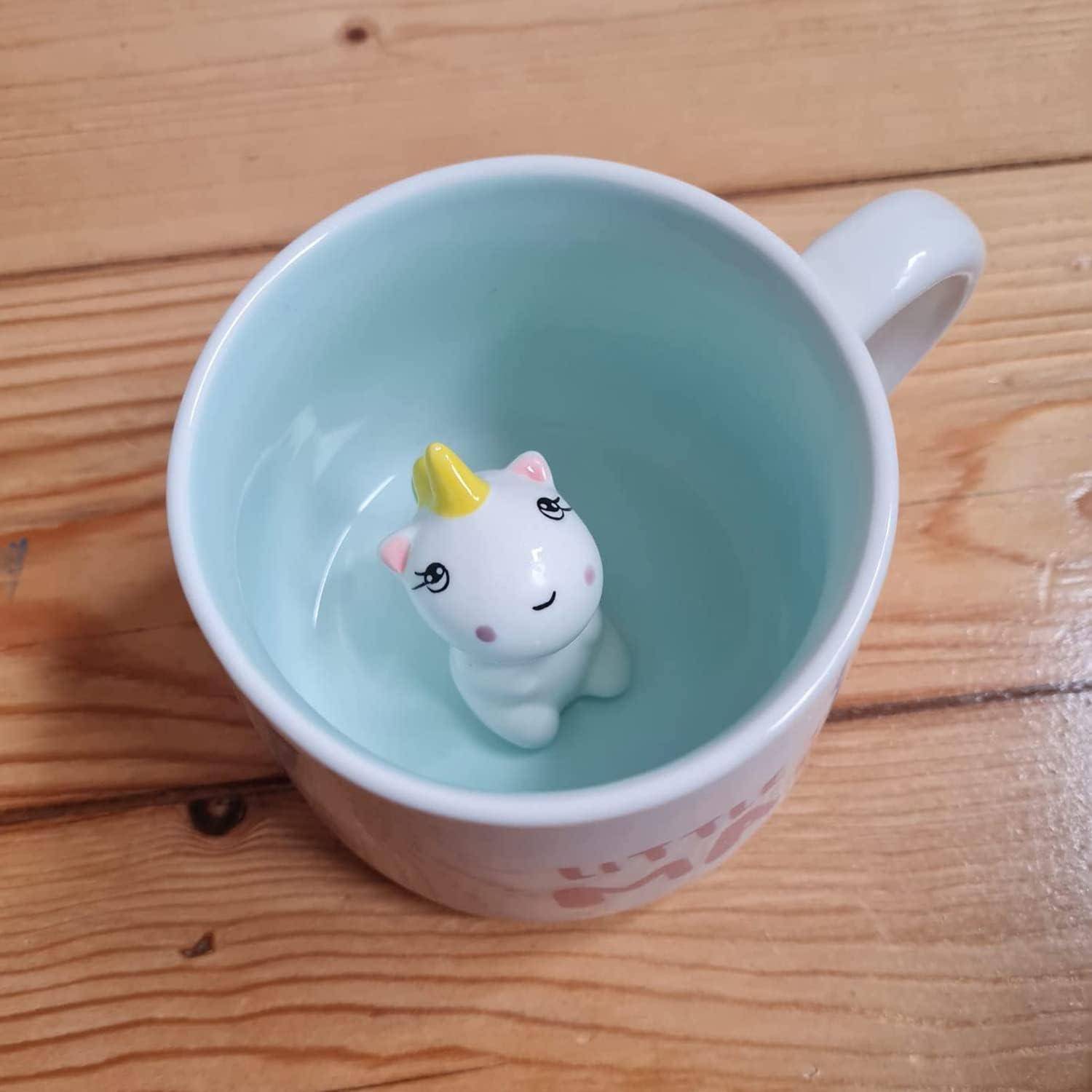 Eine Einhornfigur mit einem gelben Horn ist in einer weißen Tasse befestigt, die auf einem Holztisch steht.