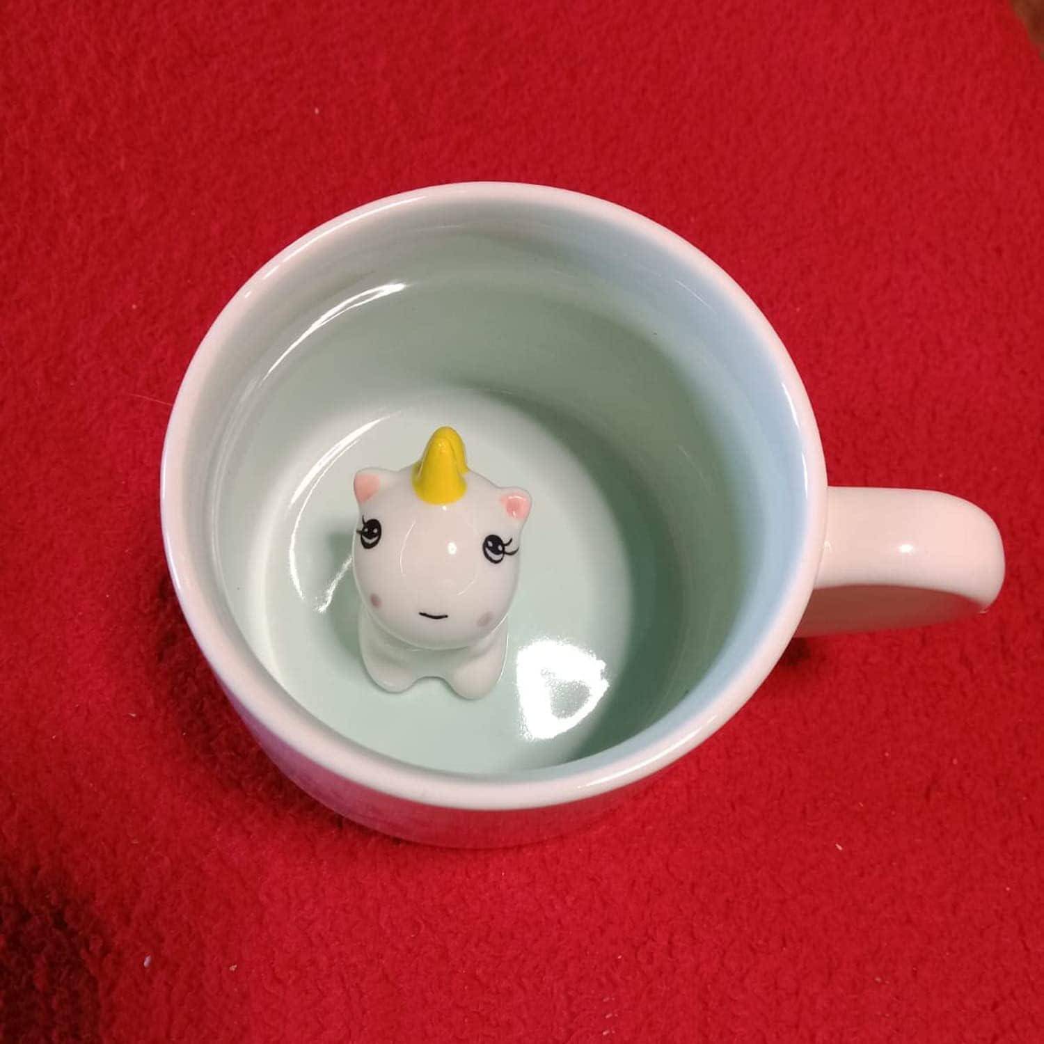 Eine weiße Tasse auf einer roten Oberfläche mit einer Einhorn-Figur im Inneren, sichtbar beim Hineinschauen.