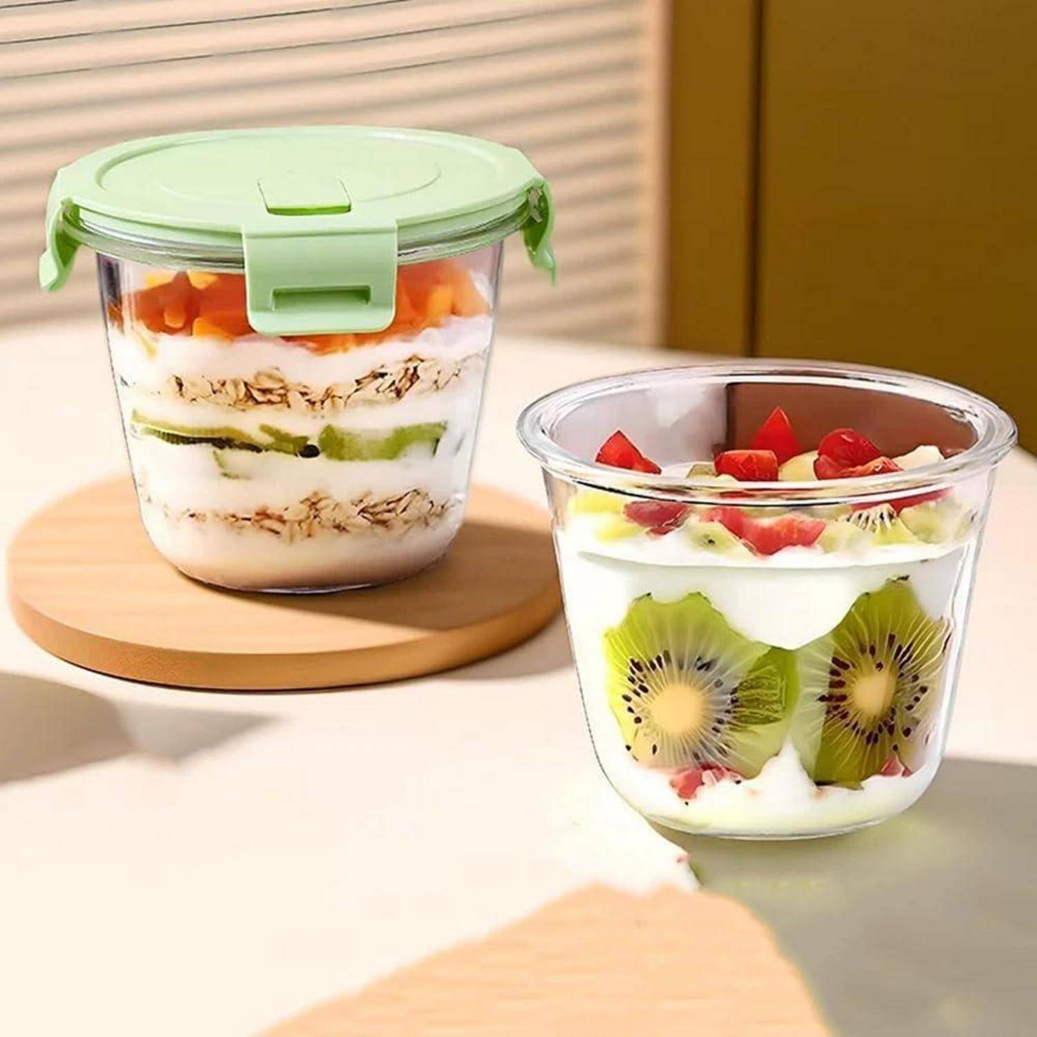 Zwei durchsichtige Behälter, einer mit einem grünen Deckel, gefüllt mit geschichteten Joghurt, Granola und verschiedenen Früchten wie Kiwi und Erdbeeren.