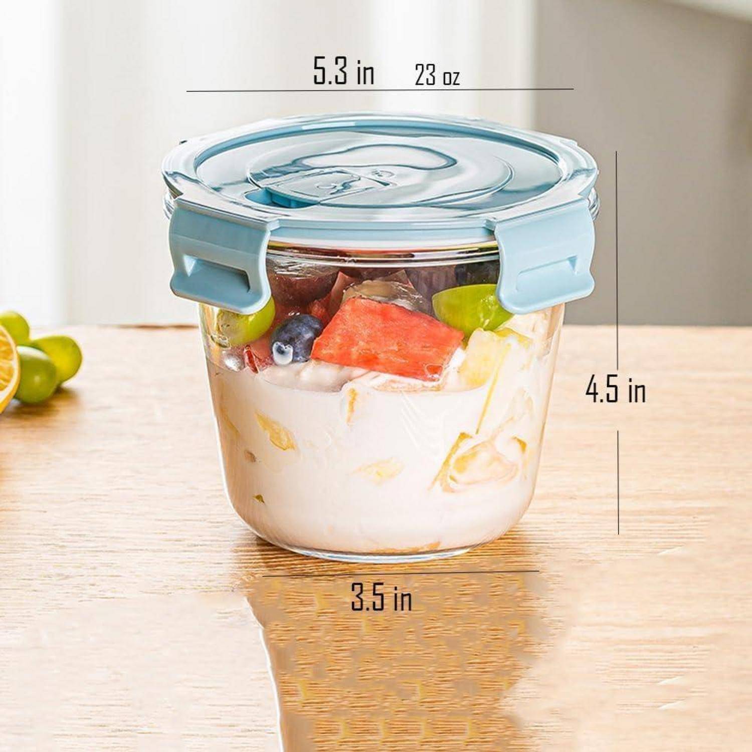 Ein transparenter Behälter enthält Joghurt mit Früchten. Deckel beschriftet mit '5,3 Zoll, 23 oz'; Höhe '4,5 Zoll'; Basisbreite '3,5 Zoll'. Limettenscheiben an der Seite.